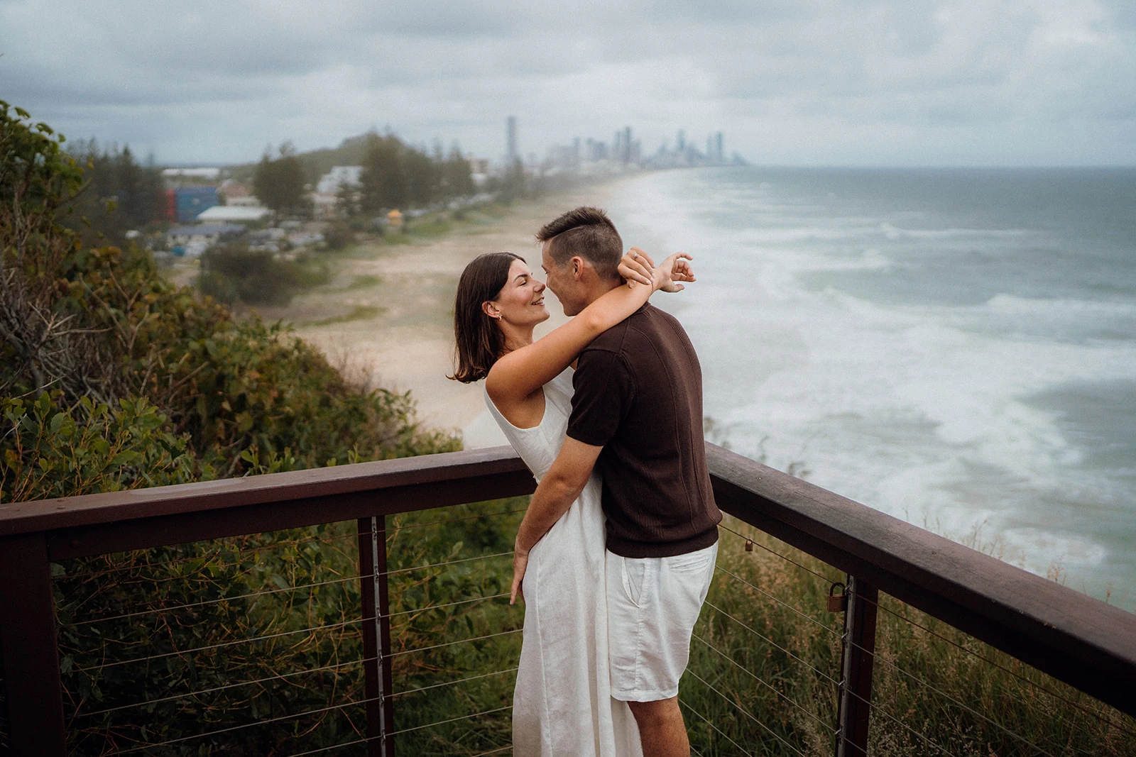 A couple embrace at a lookout above a long stretch of coastline.
