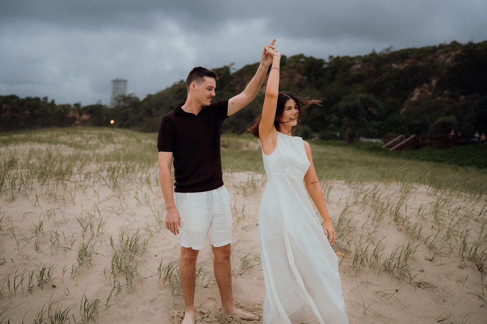 A man raises their joined hands as his partner turns among beach grasses.