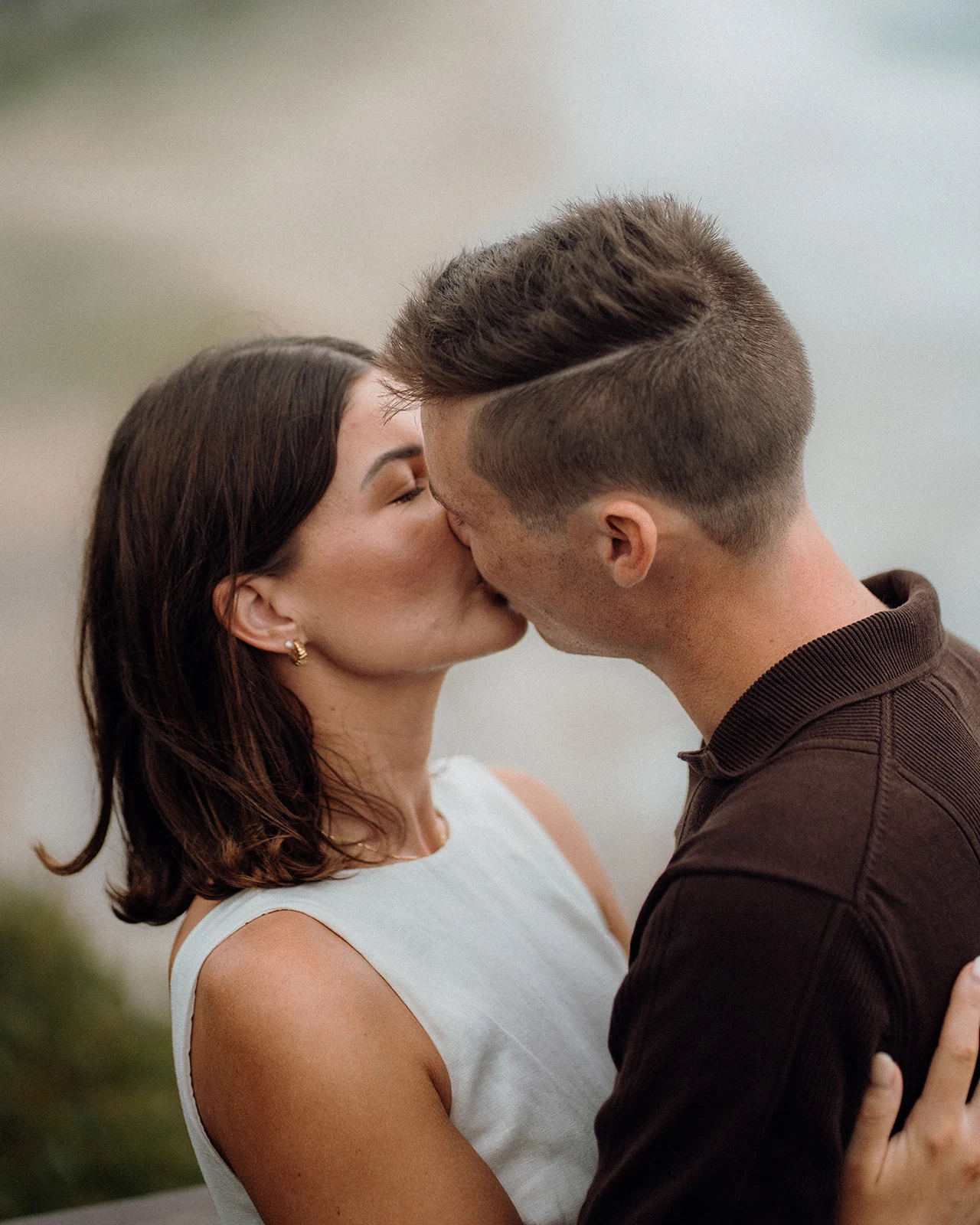 A close portrait of a couple kissing, with her hand resting on his shoulder.