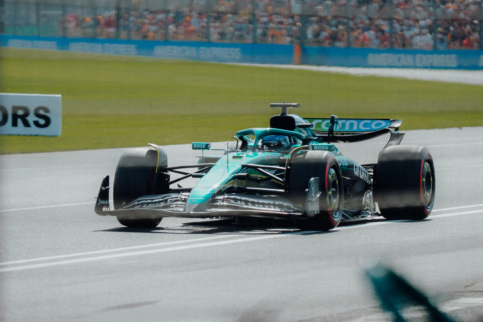 A green Formula 1 car approaches a bend in front of a packed grandstand.