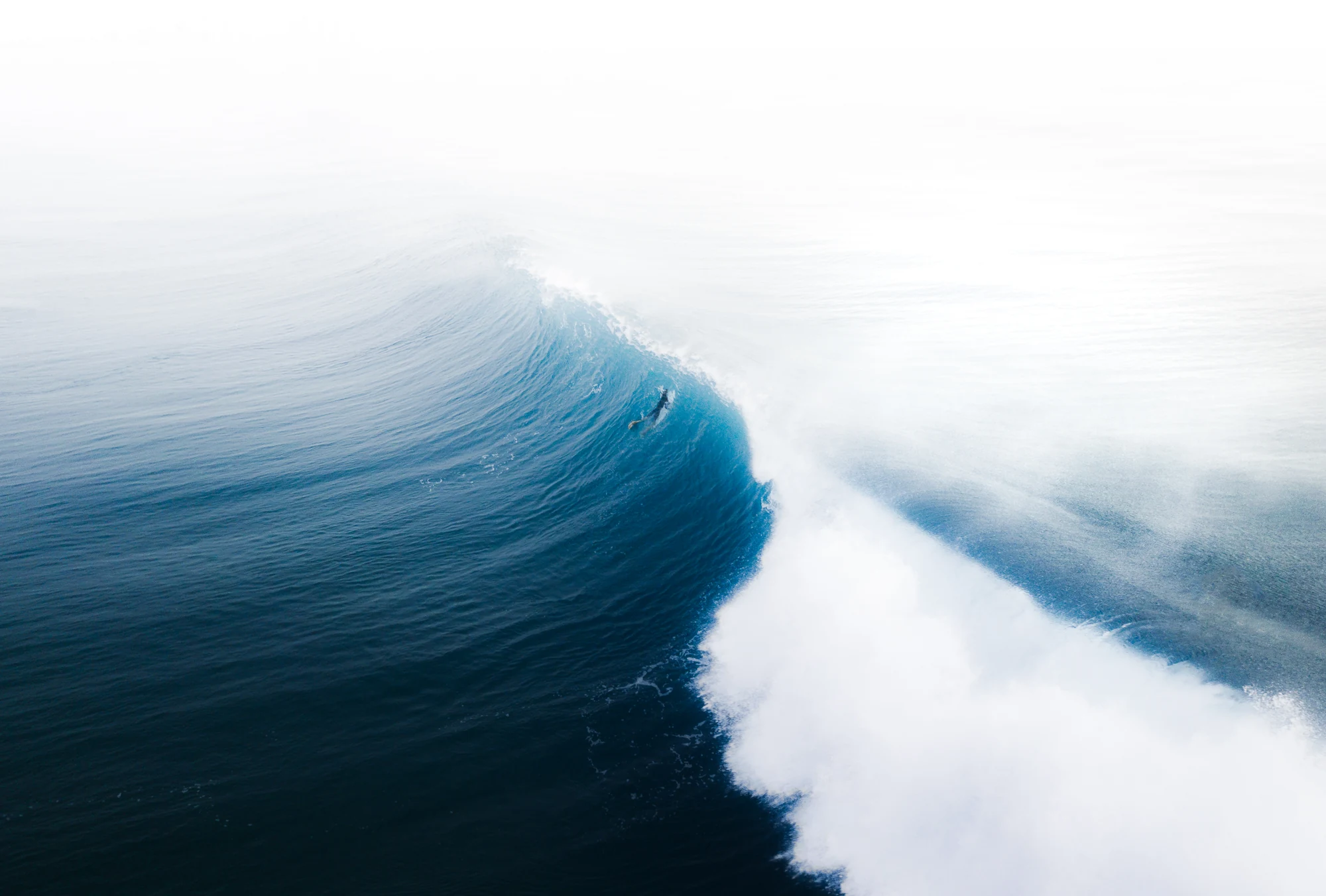 A blue wave curls beneath a veil of windblown white spray.