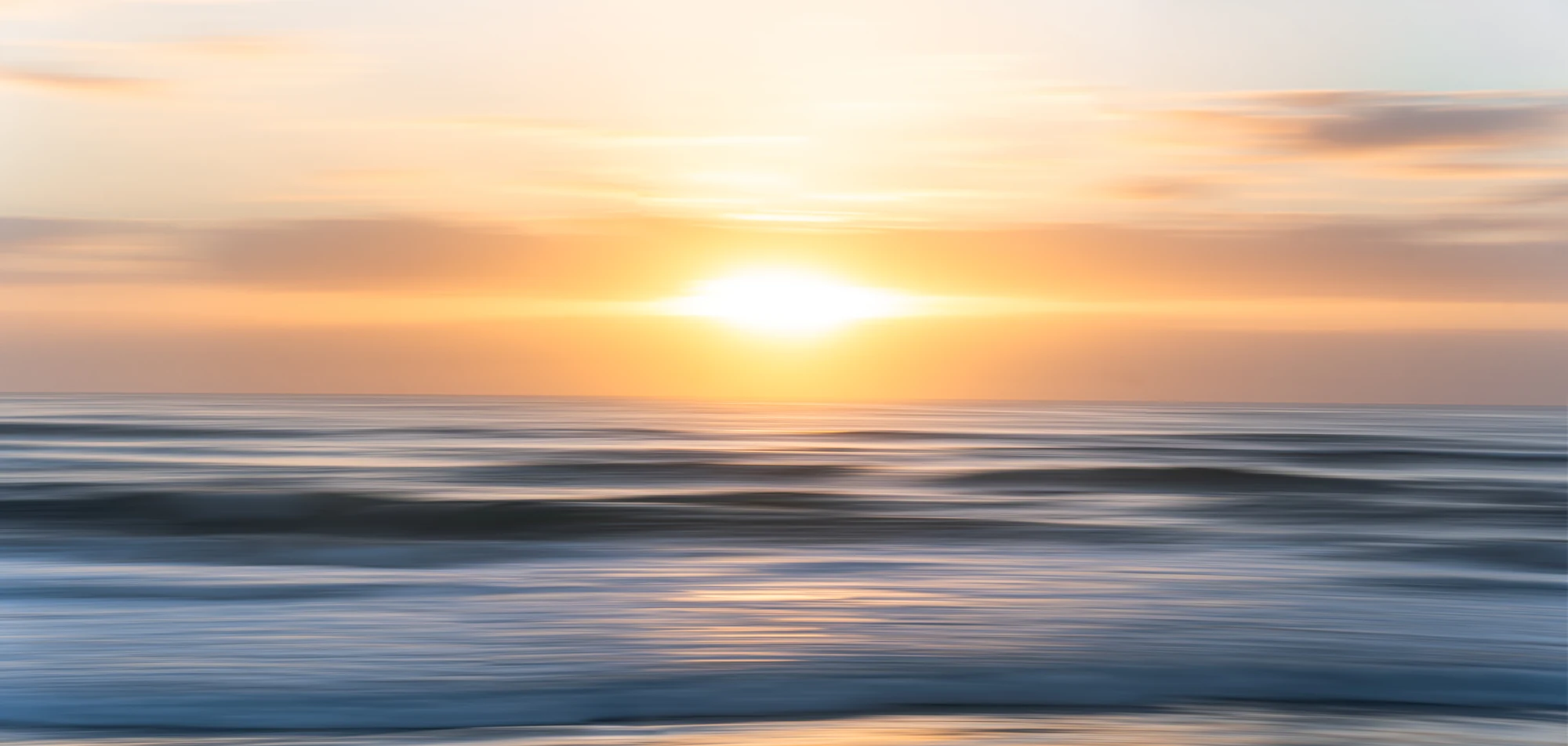 Soft horizontal bands of orange sunrise and blue sea form an abstract coastal image.