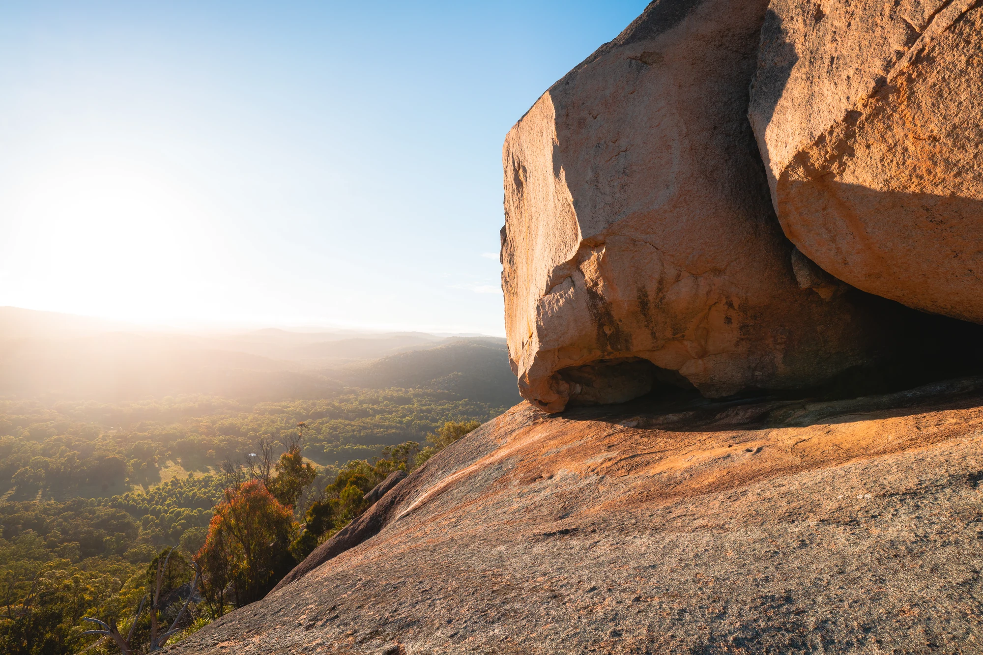 Warm light falls on a massive granite boulder above a forested valley.