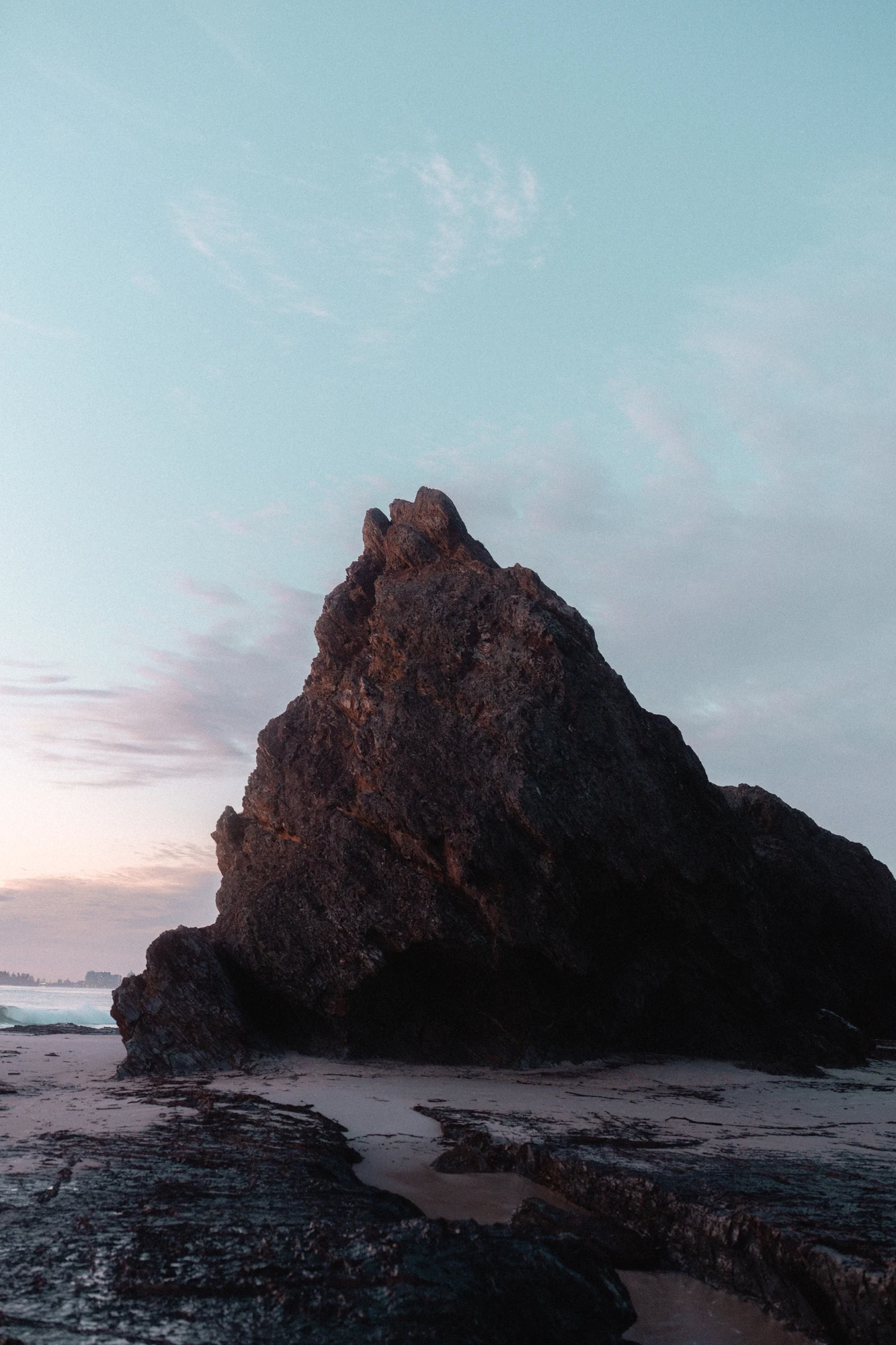 A solitary sea stack rises from pale water beneath a pastel sky.