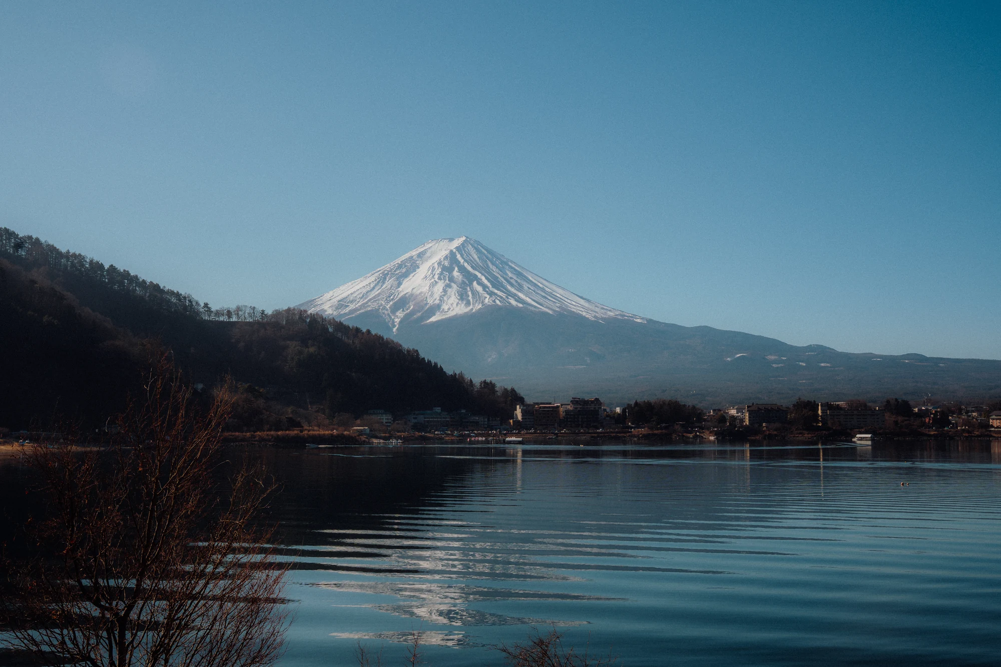 Snow-covered Mount Fuji rises above a calm lake with a soft reflection.