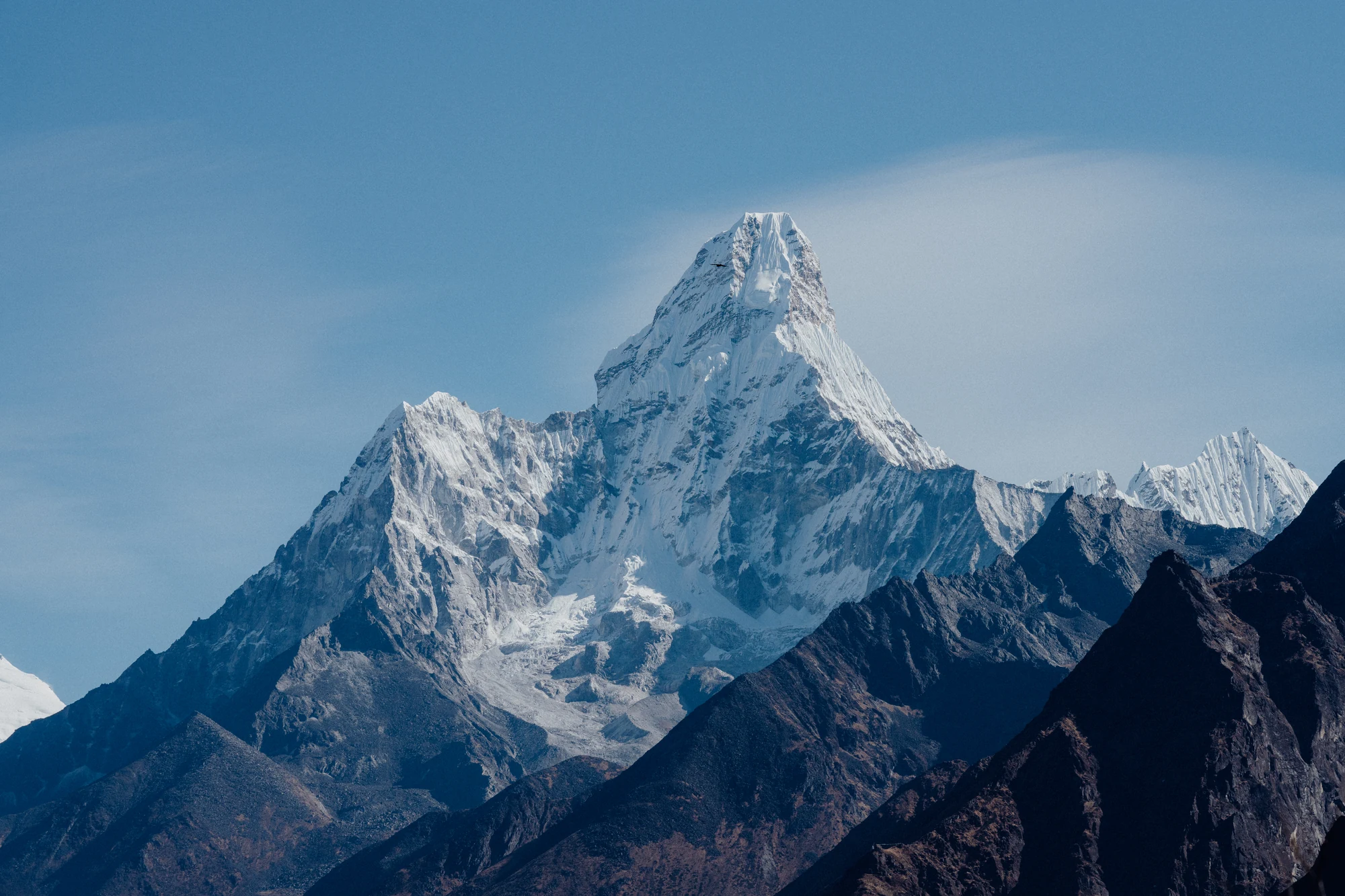 A sharply defined snow-covered mountain towers above darker overlapping ridges.