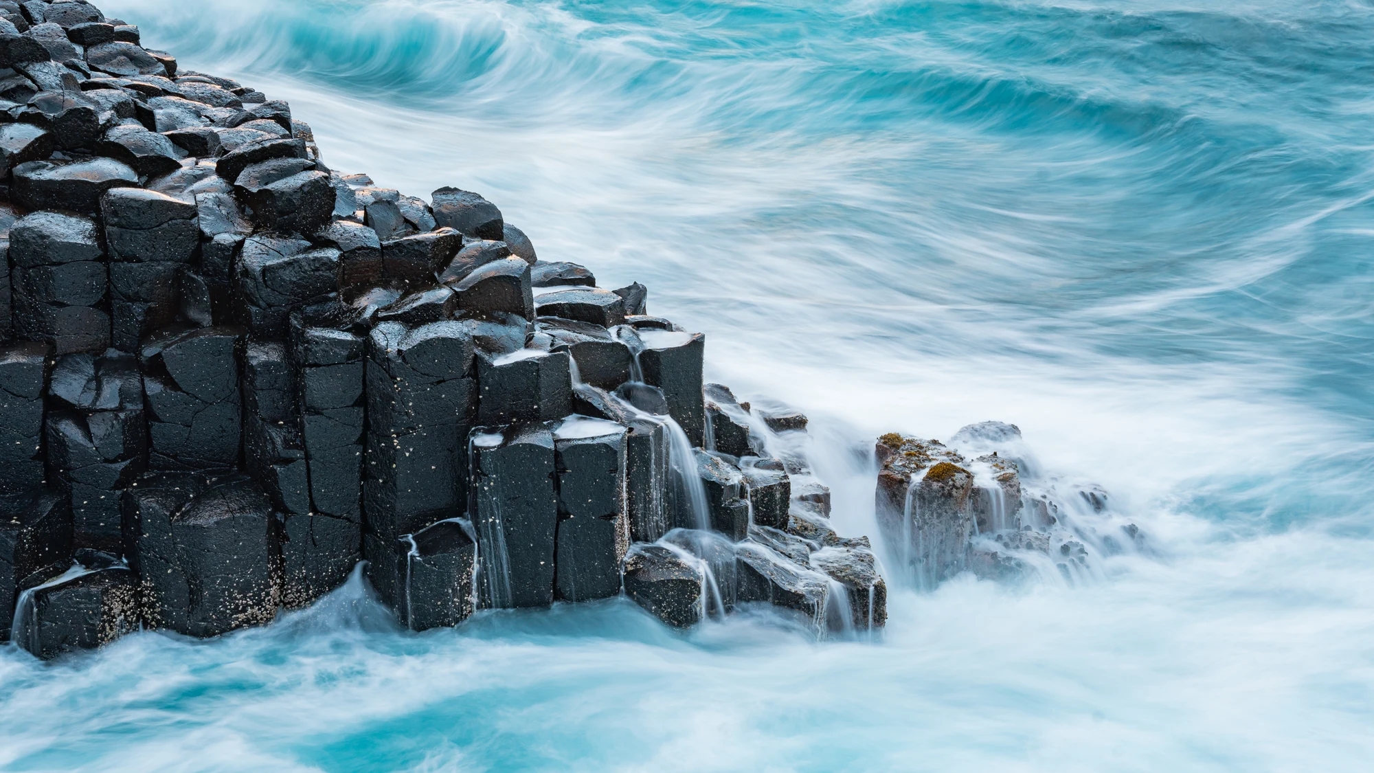 Silky turquoise surf spills around dark geometric basalt columns.