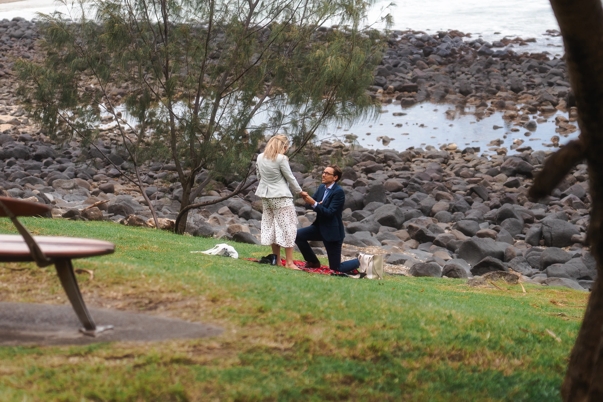 A man proposes on a grassy headland above a rocky beach.