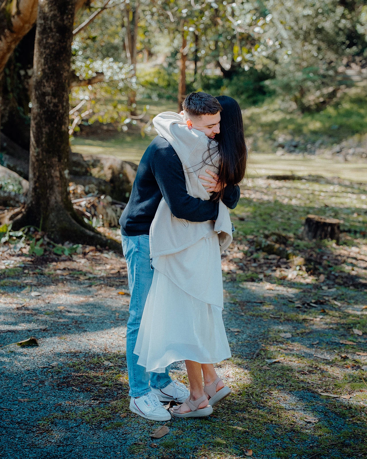 A couple hold each other tightly in the shade of a large tree.