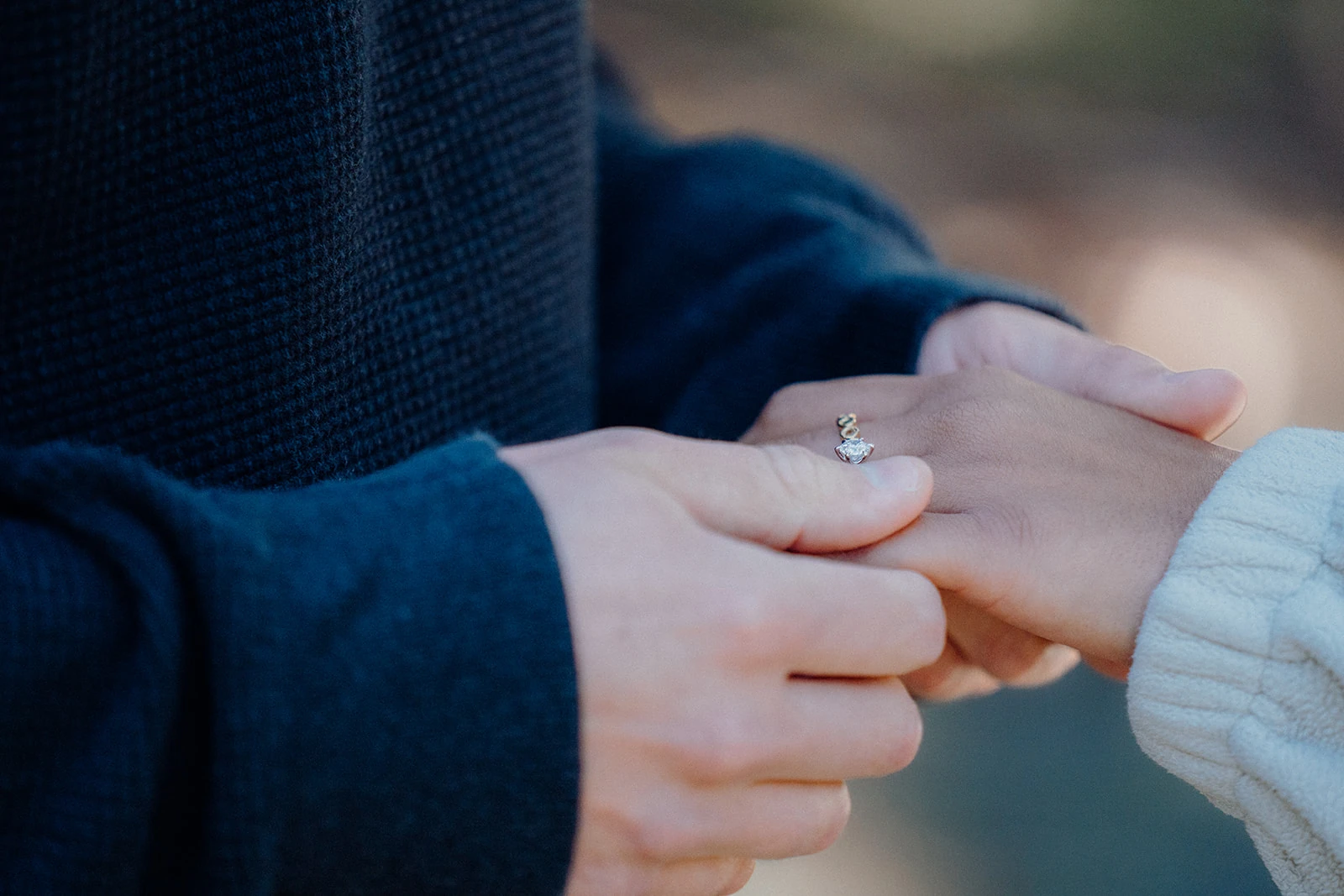 A man gently holds his partner's hand with her engagement ring.