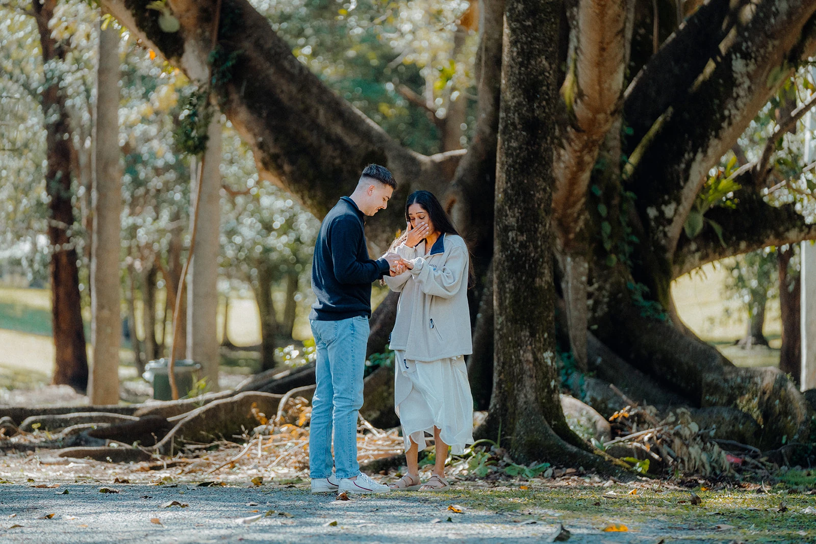 A couple look down at the ring together beneath the trees.