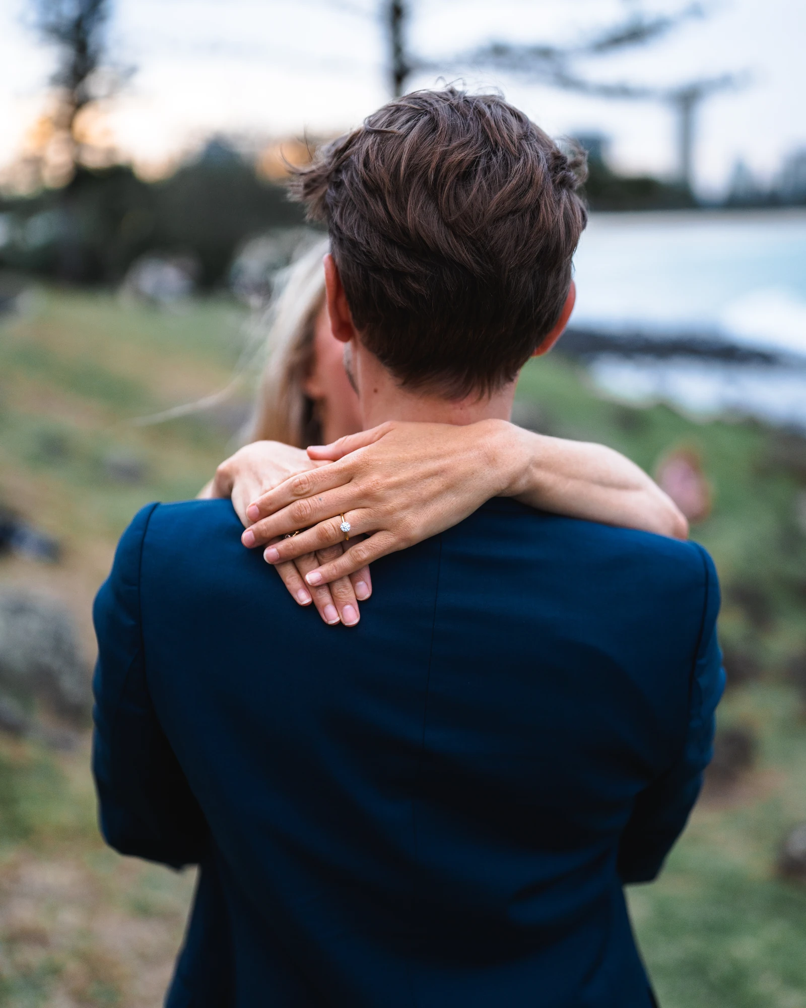 An engagement ring rests against a man's neck as his partner embraces him.