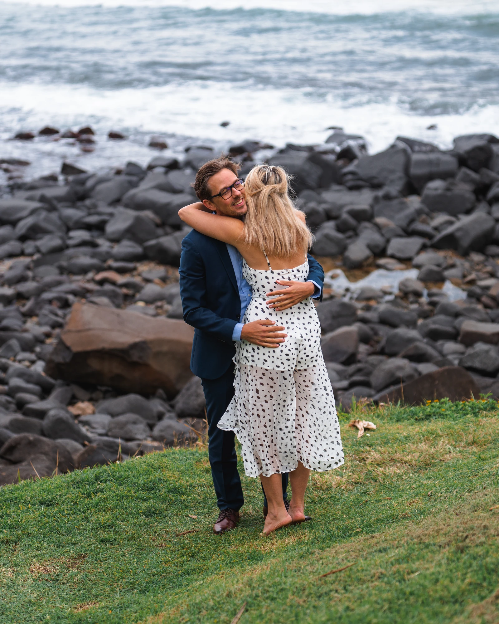A couple laugh in an embrace above the rocky shoreline.
