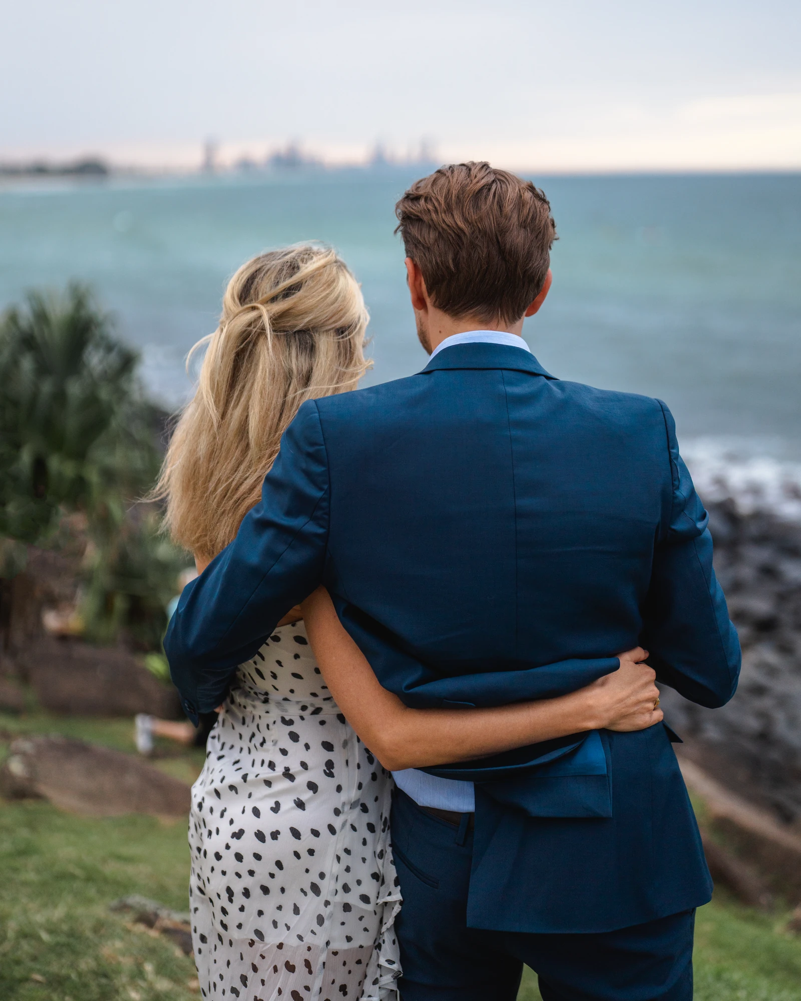A couple look out across the bay with their arms around each other.