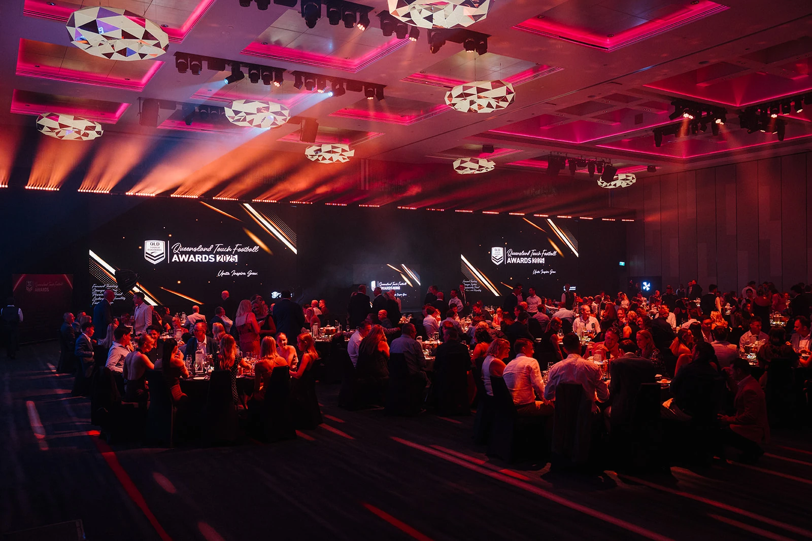 Guests fill a ballroom lit in pink and amber at an awards evening.