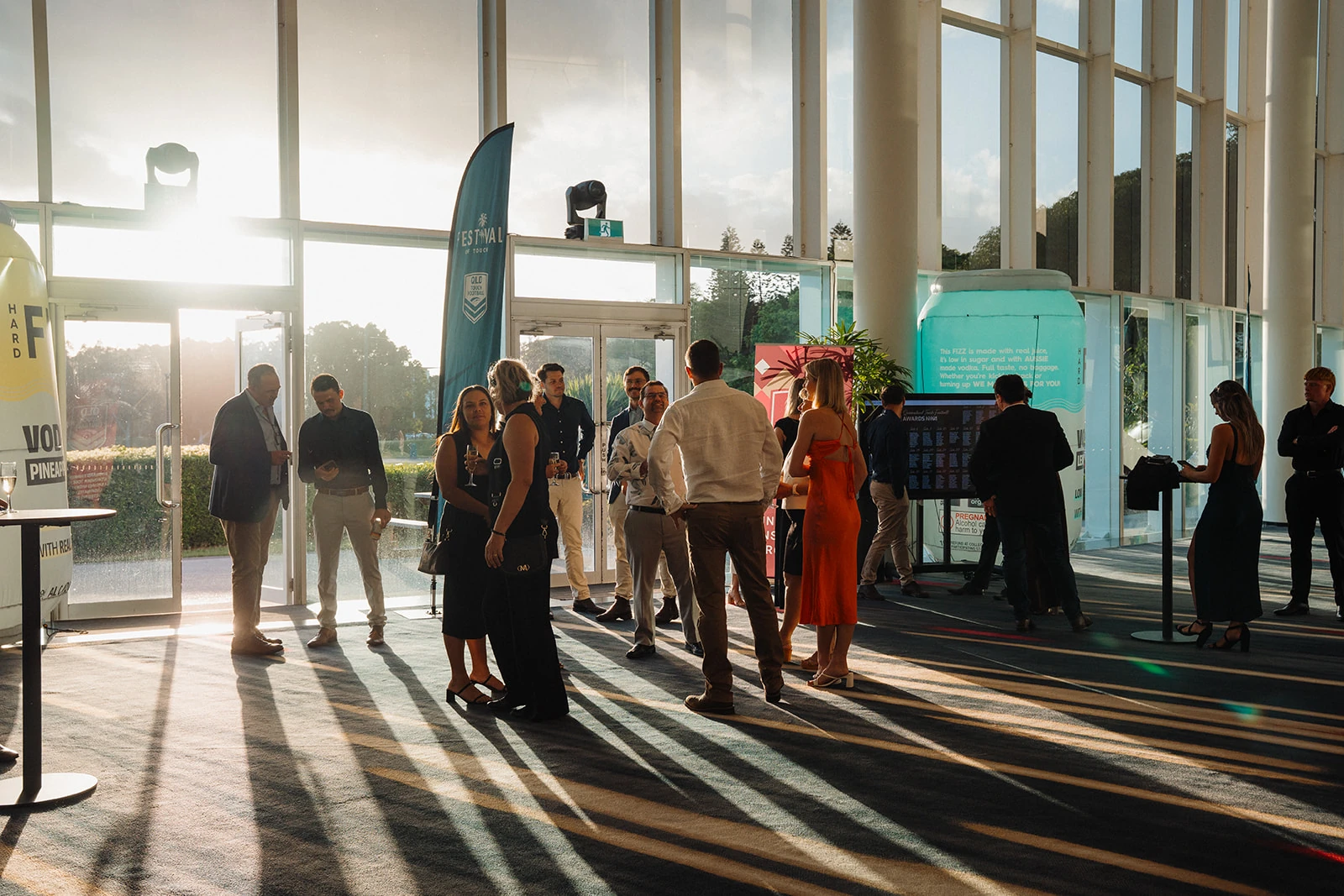 Guests mingle in a venue foyer as evening light falls through tall windows.