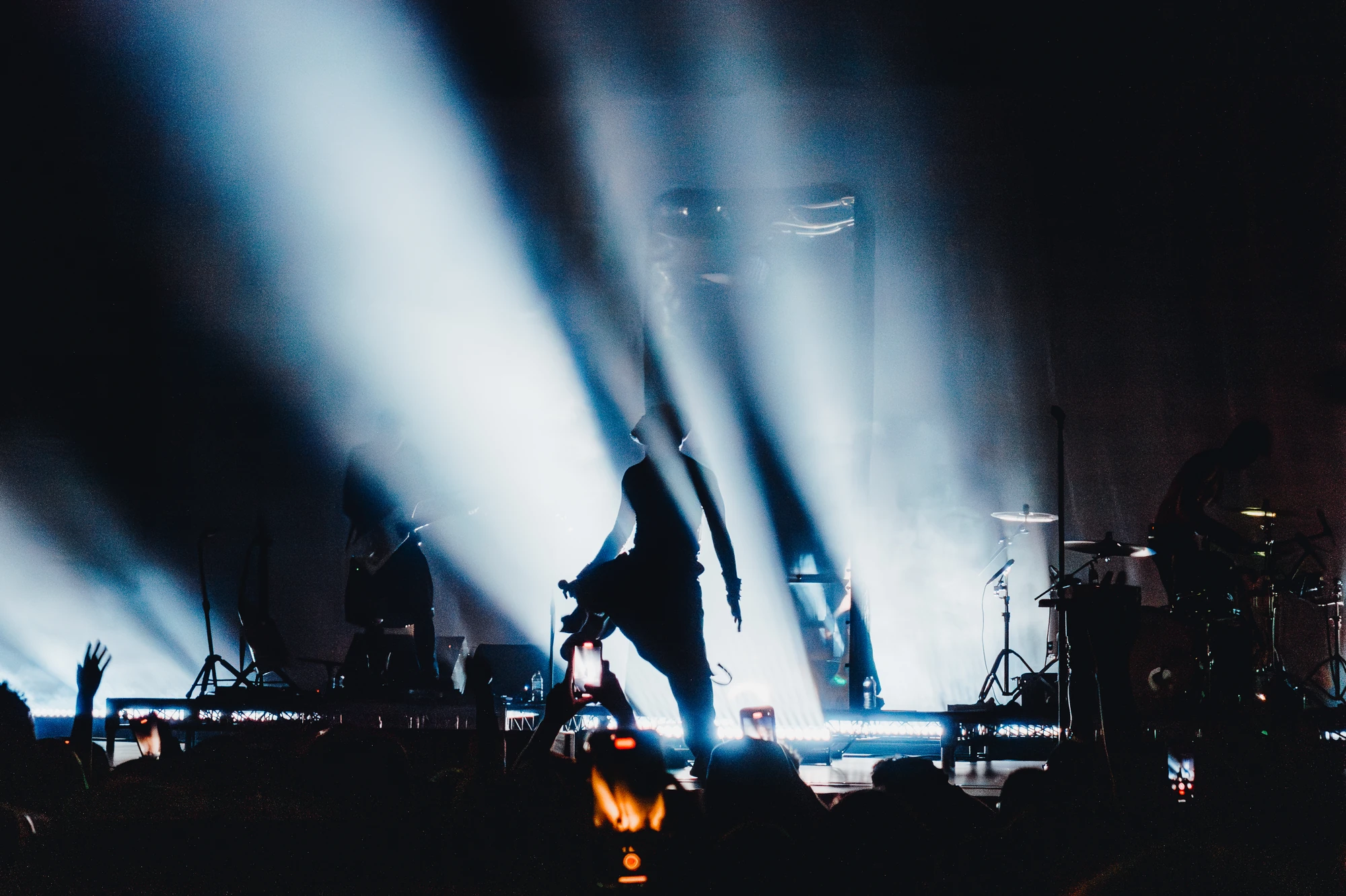 A performer steps across the stage between tall white beams of light.