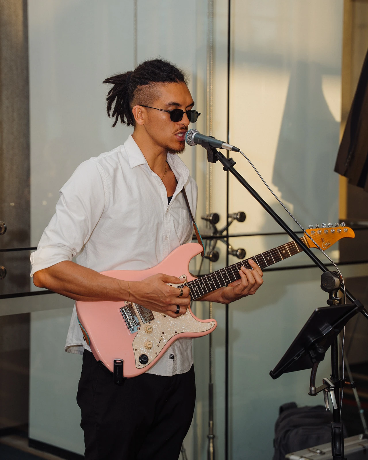 A musician sings into a microphone while playing a pink electric guitar.