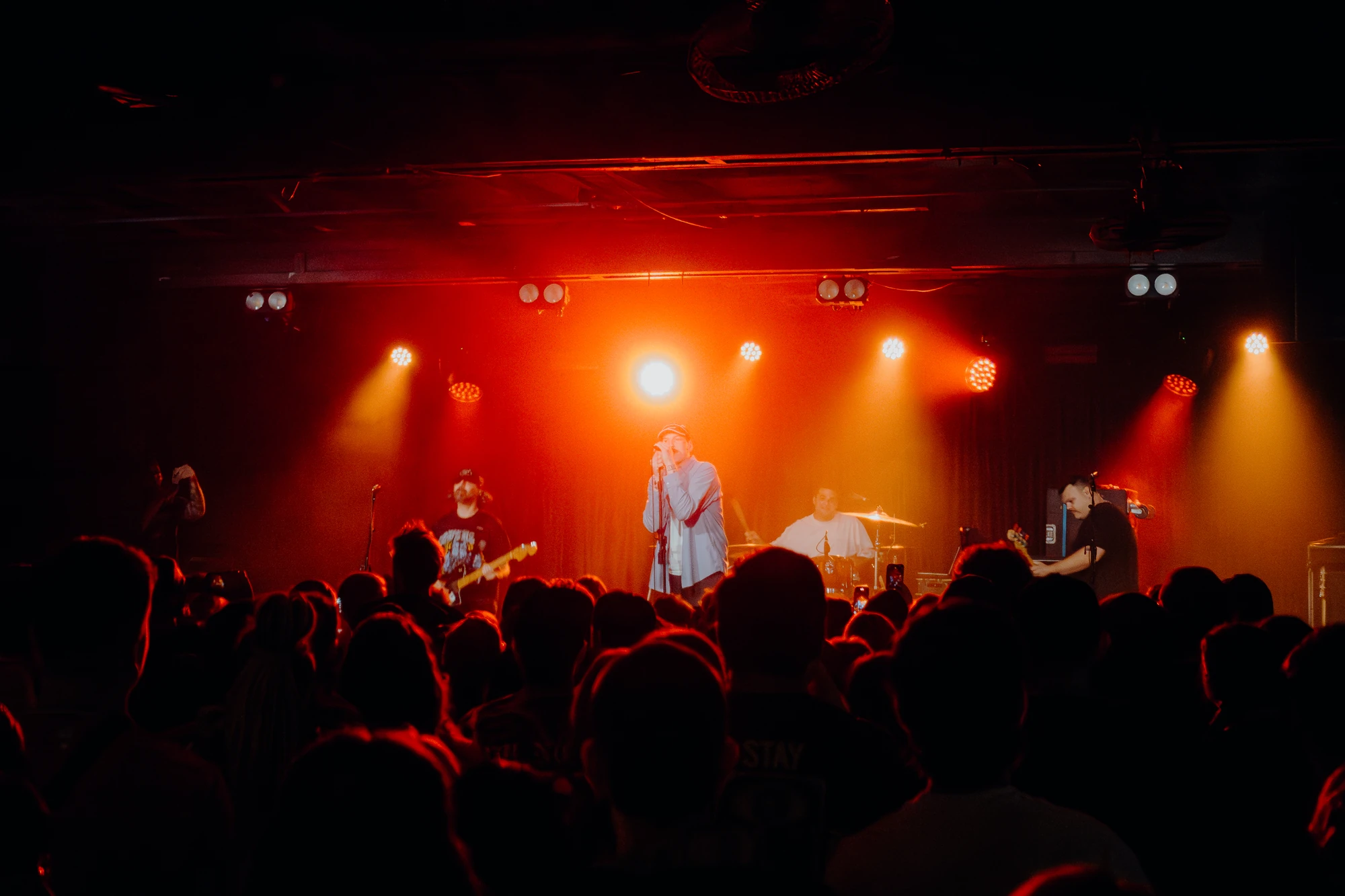 A band performs beneath red and amber lights above a crowded audience.