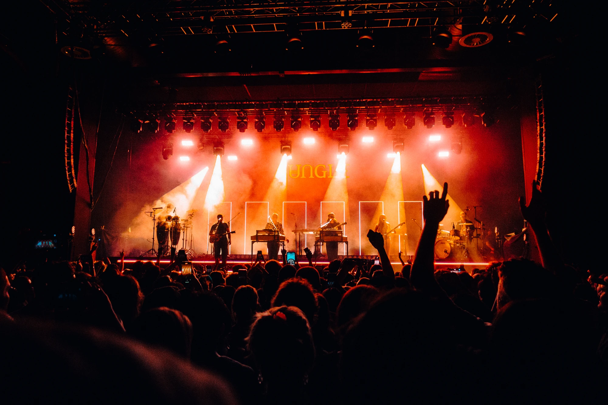 A raised hand rises above a concert crowd under amber stage lights.