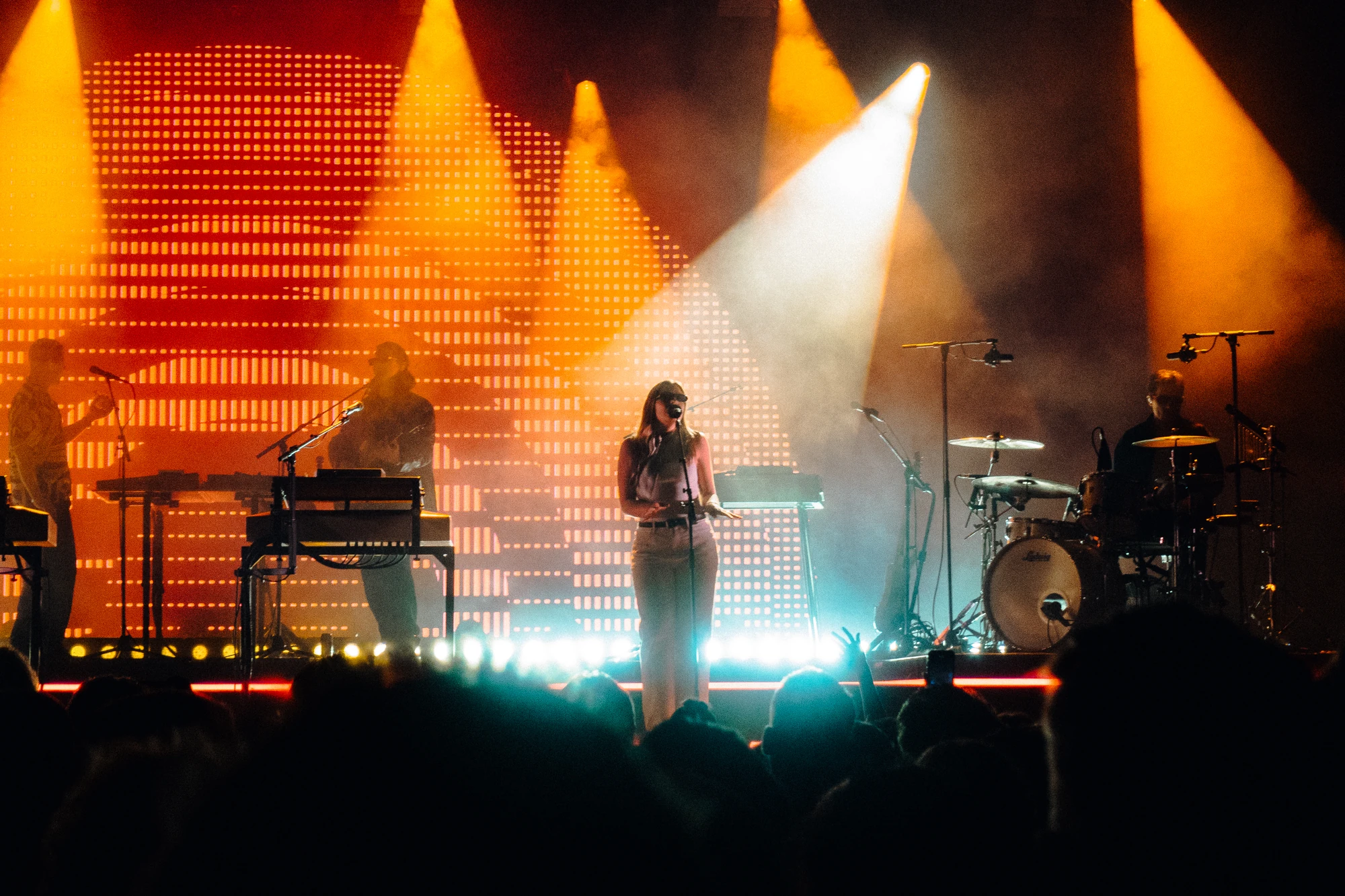 A singer performs between musicians beneath amber and white spotlights.