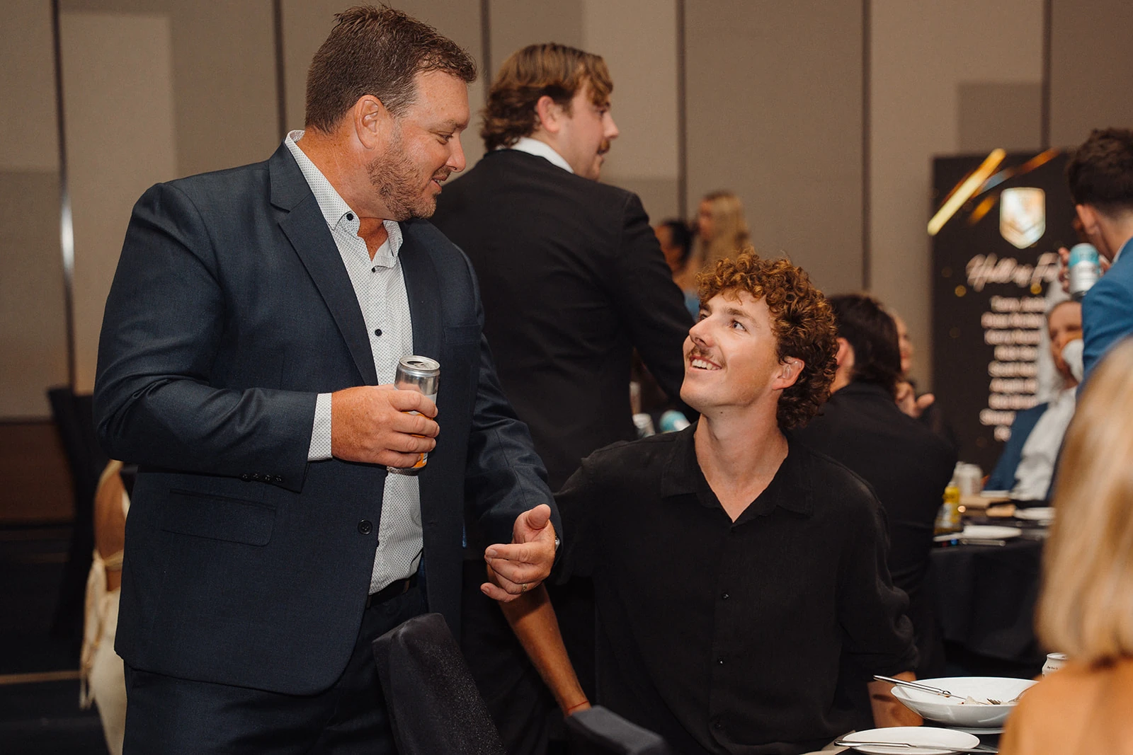Two guests smile at one another in conversation beside a dining table.