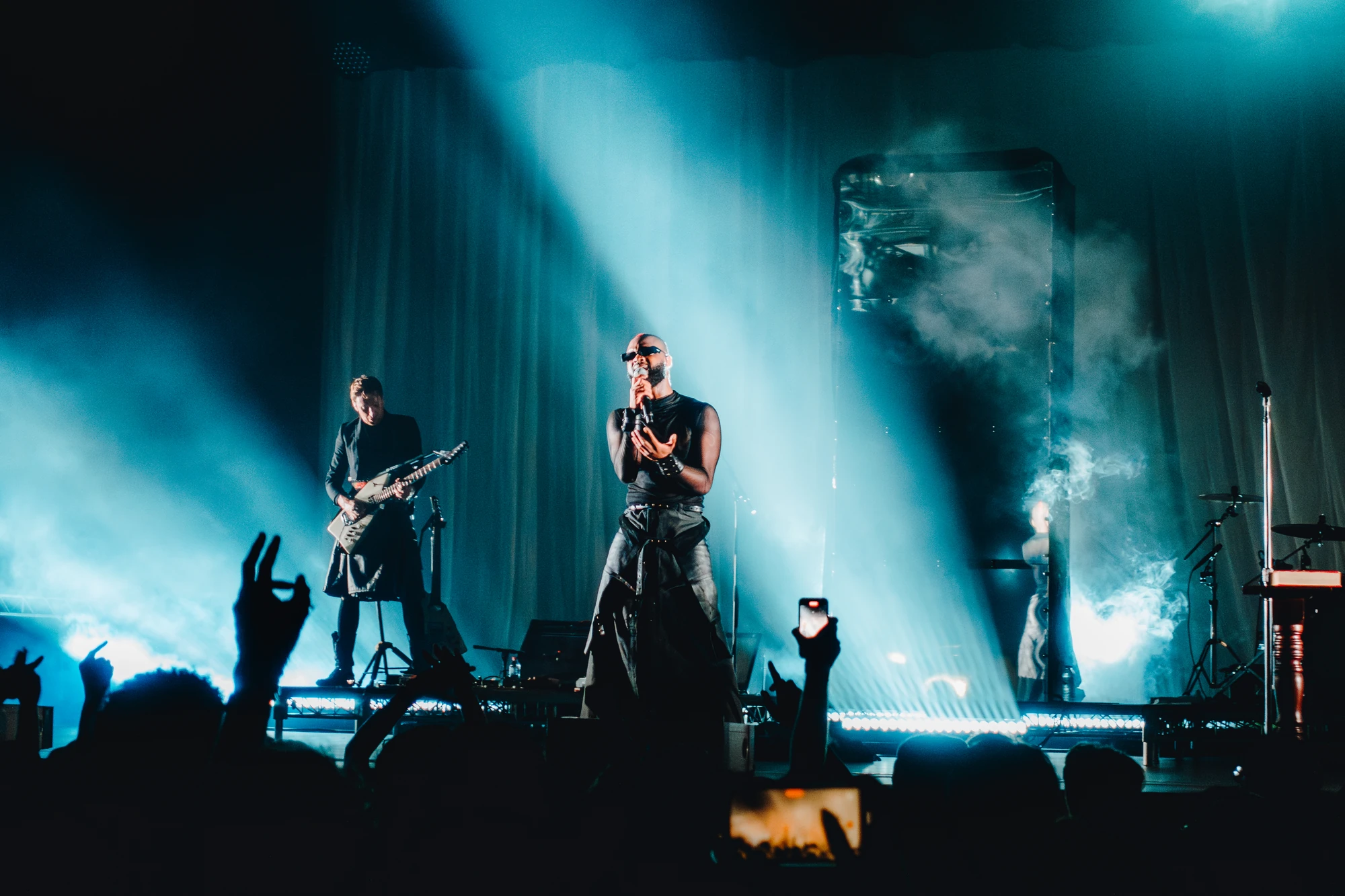 A singer and guitarist perform against tall columns of blue light.