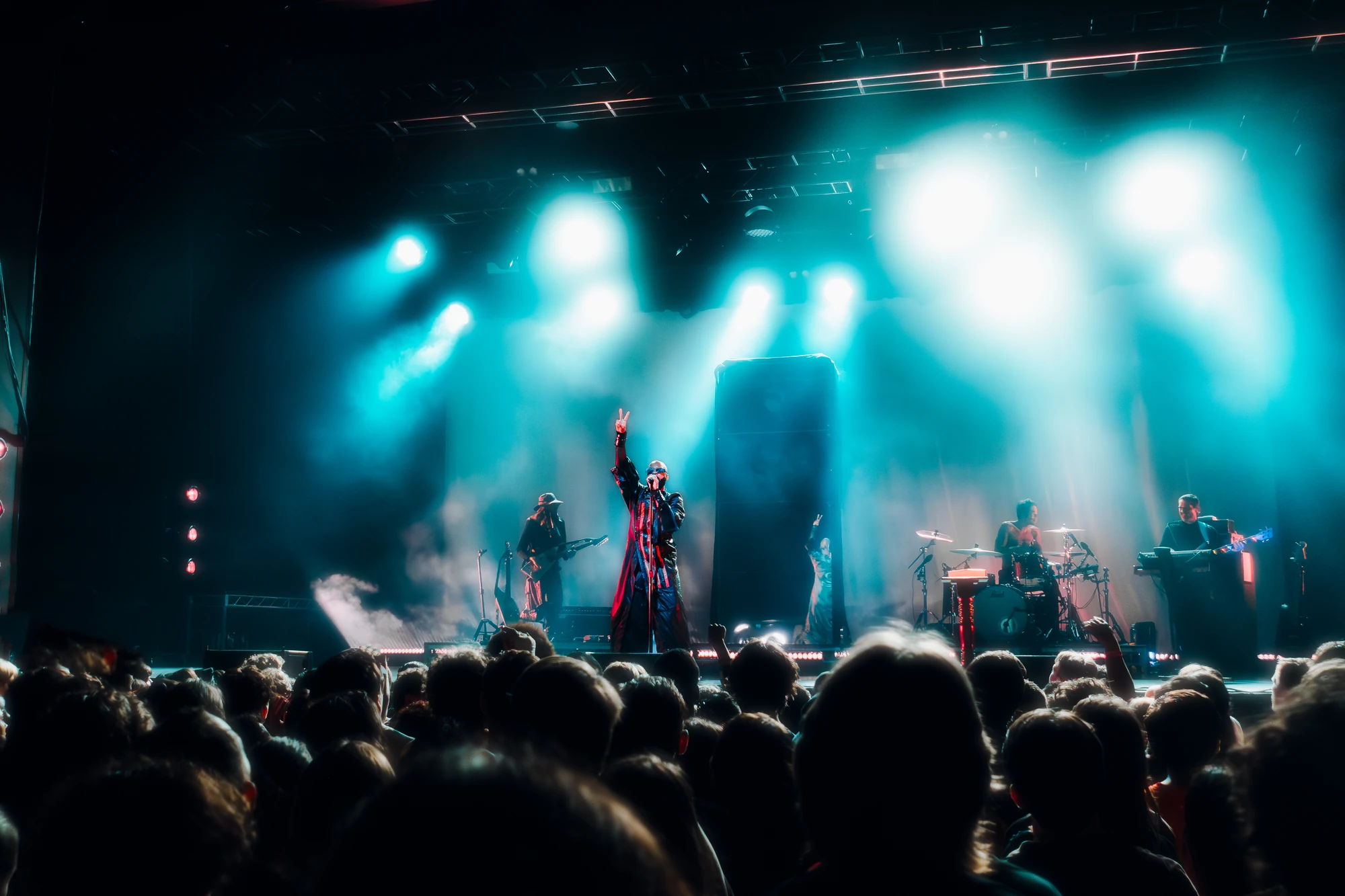 A singer raises one arm above a crowd beneath cyan stage lights.