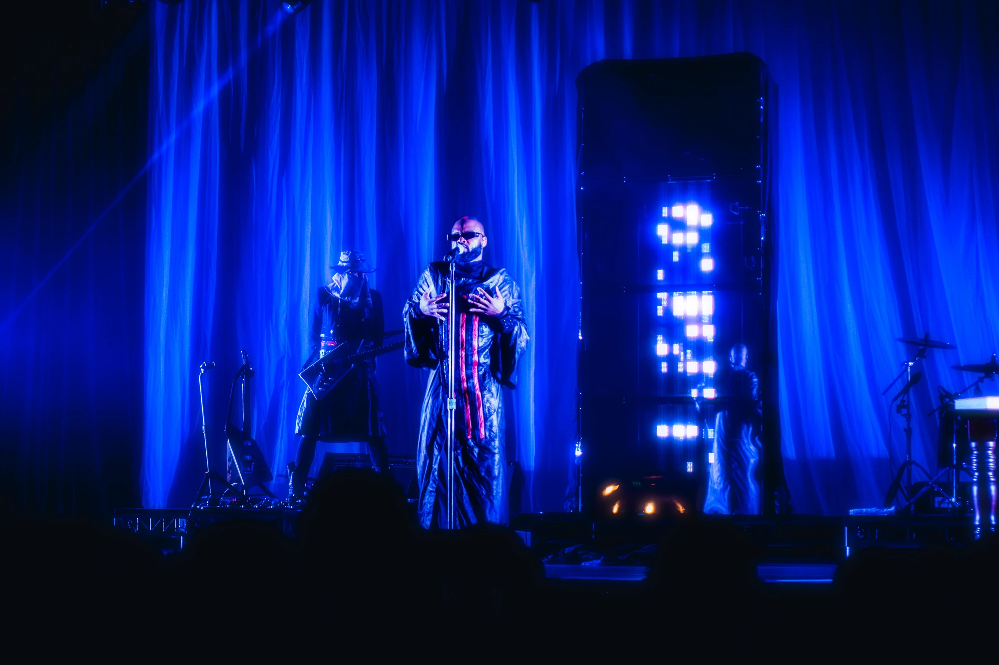 A singer in a patterned robe performs beneath blue stage lights.