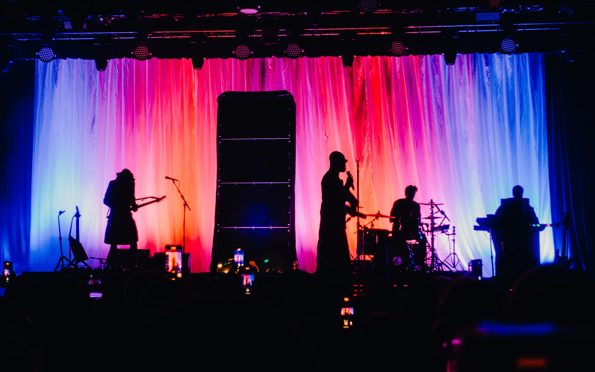 Band members are silhouetted against pink and blue curtains of light.