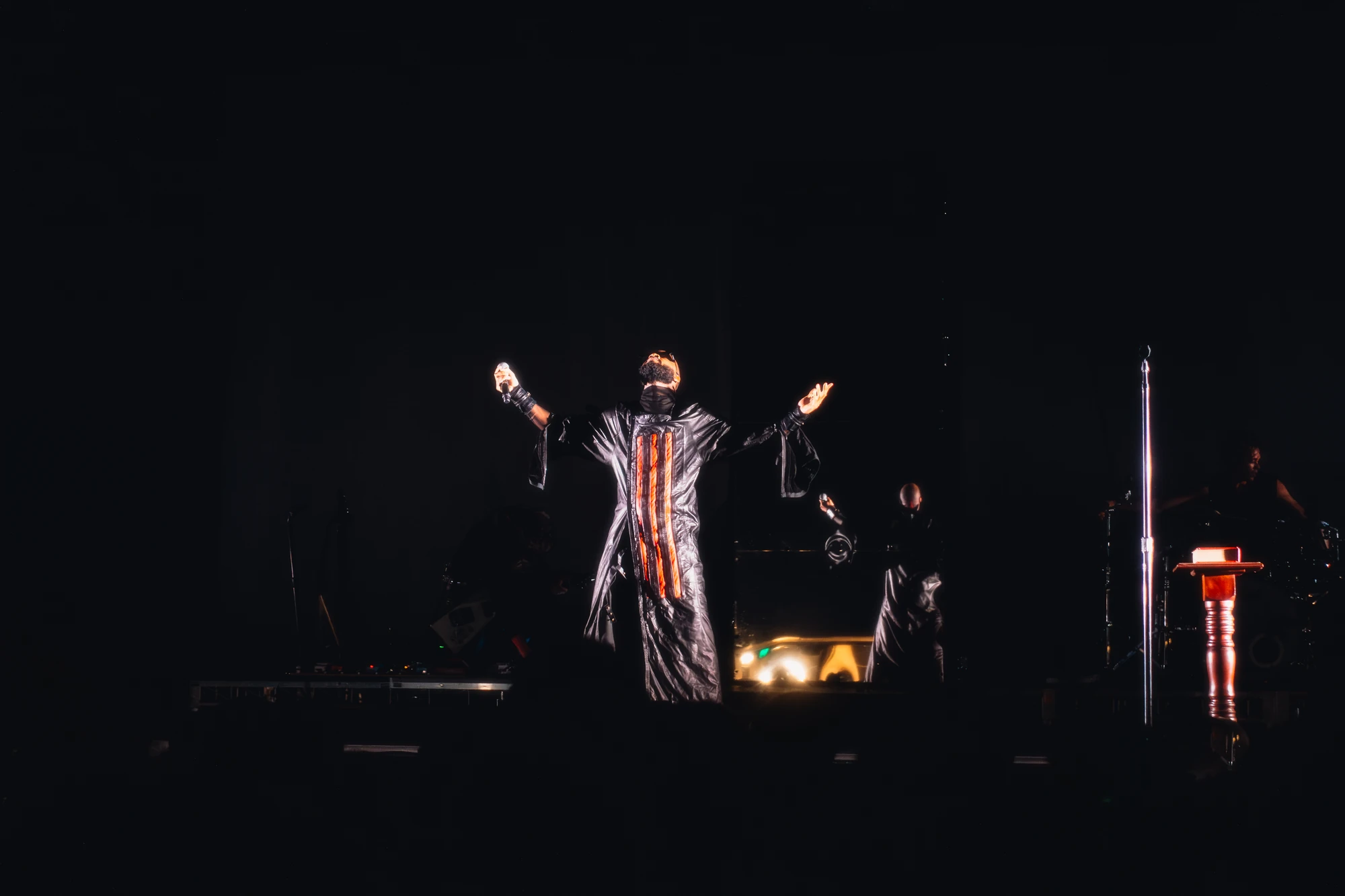 A singer spreads both arms on an otherwise dark stage.