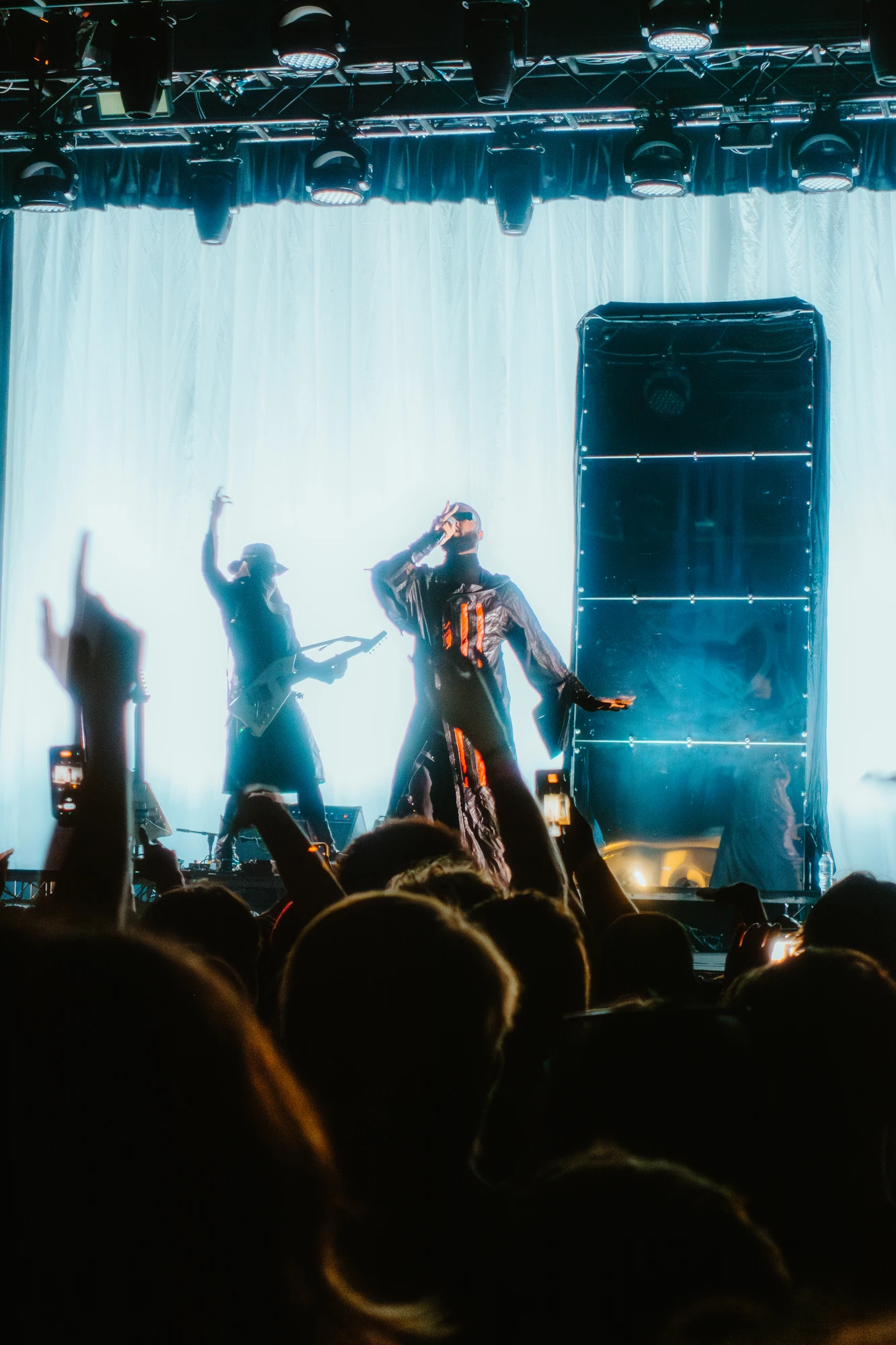A singer performs in front of a bright white backdrop and concert crowd.