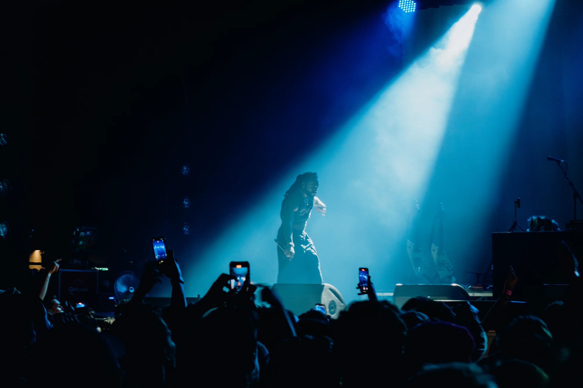 A performer stands beneath a single blue spotlight above a concert crowd.
