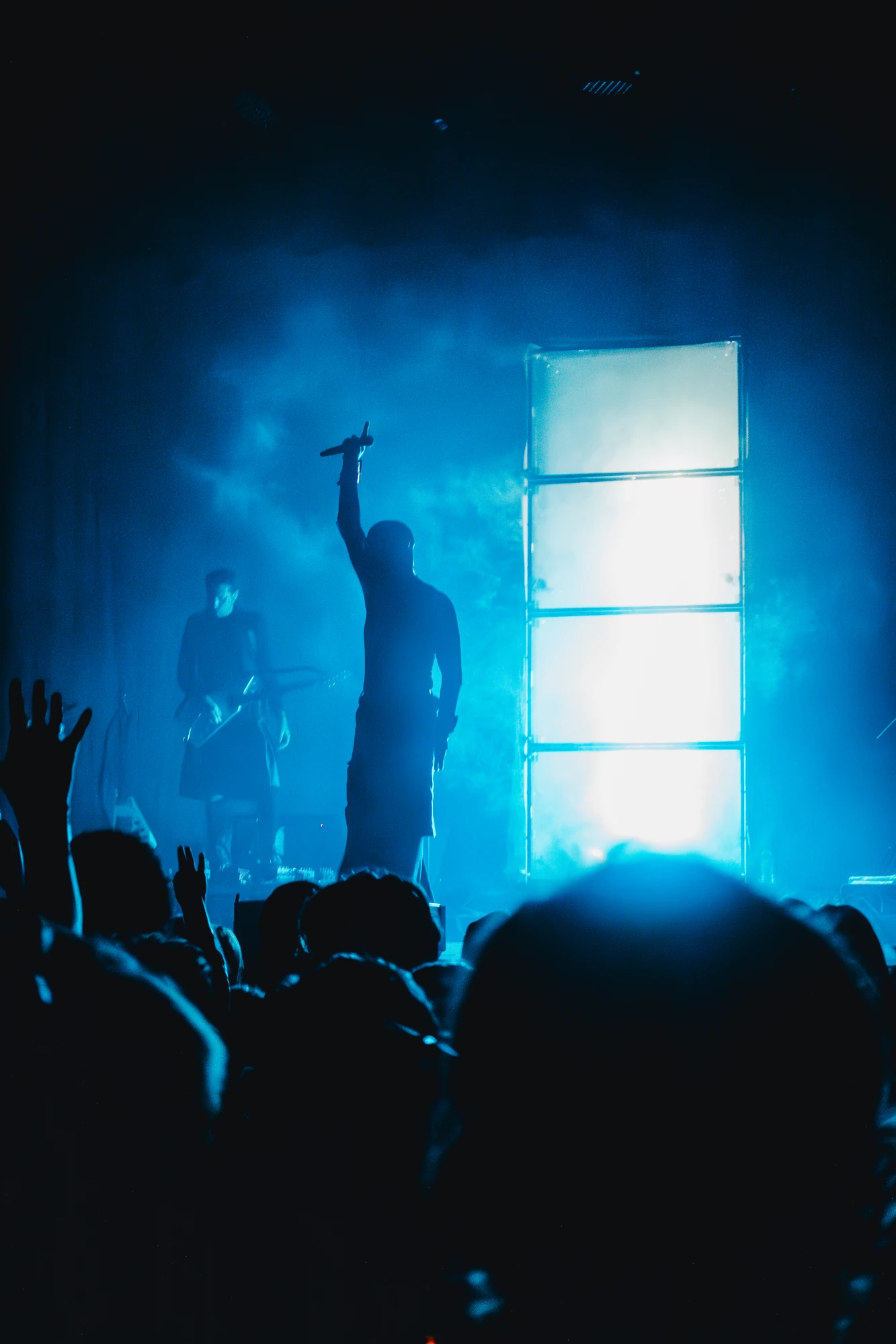 A singer raises a microphone above the crowd in blue stage light.