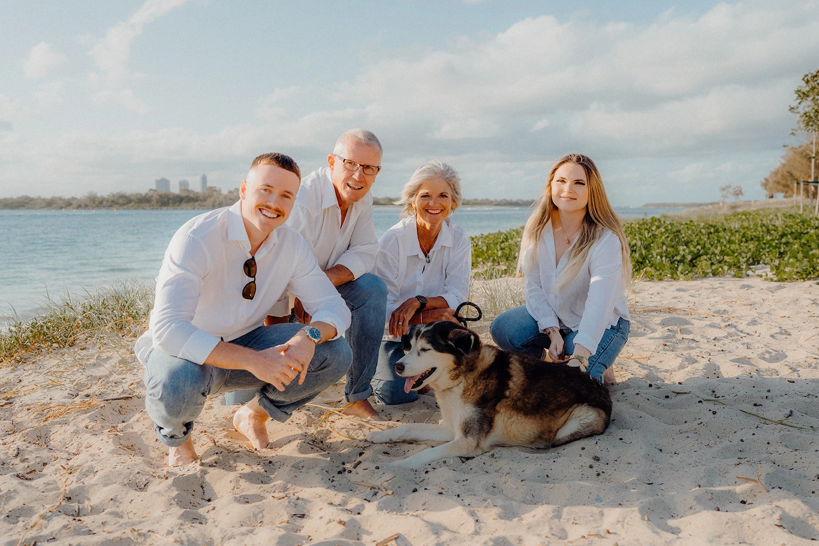 Four family members crouch beside their dog on a sandy beach.