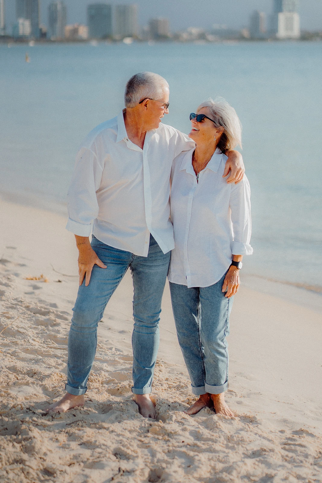An older couple look at each other with their arms around one another.