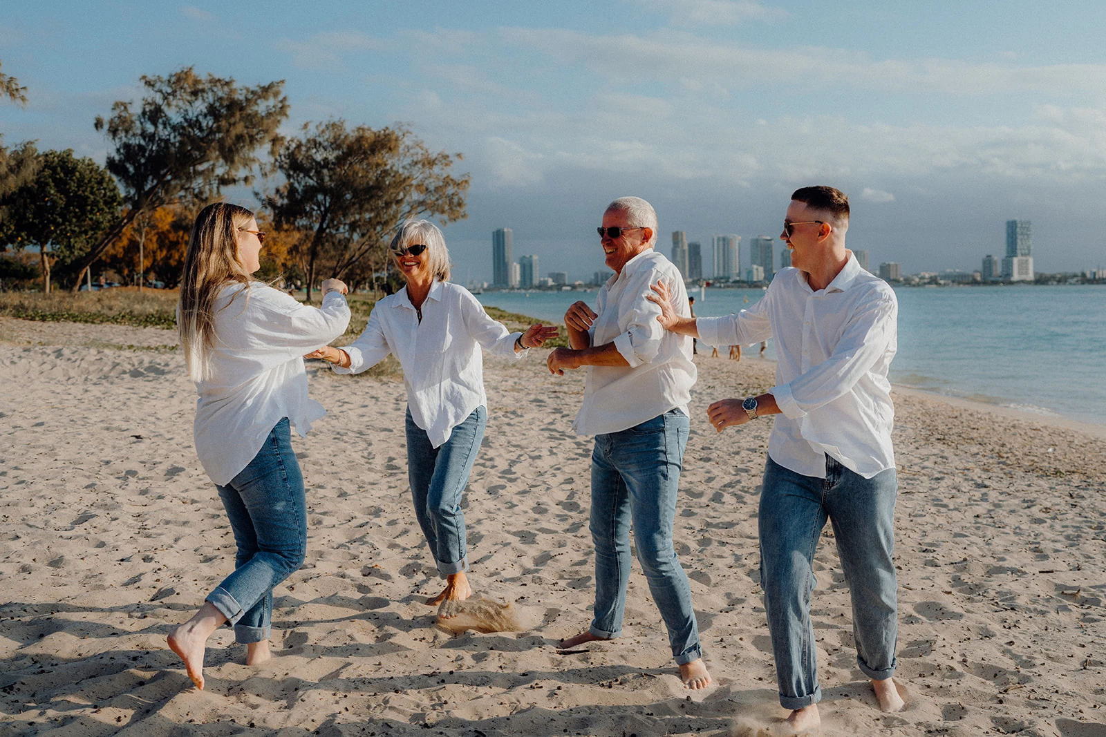 Four family members laugh and turn toward one another on the sand.
