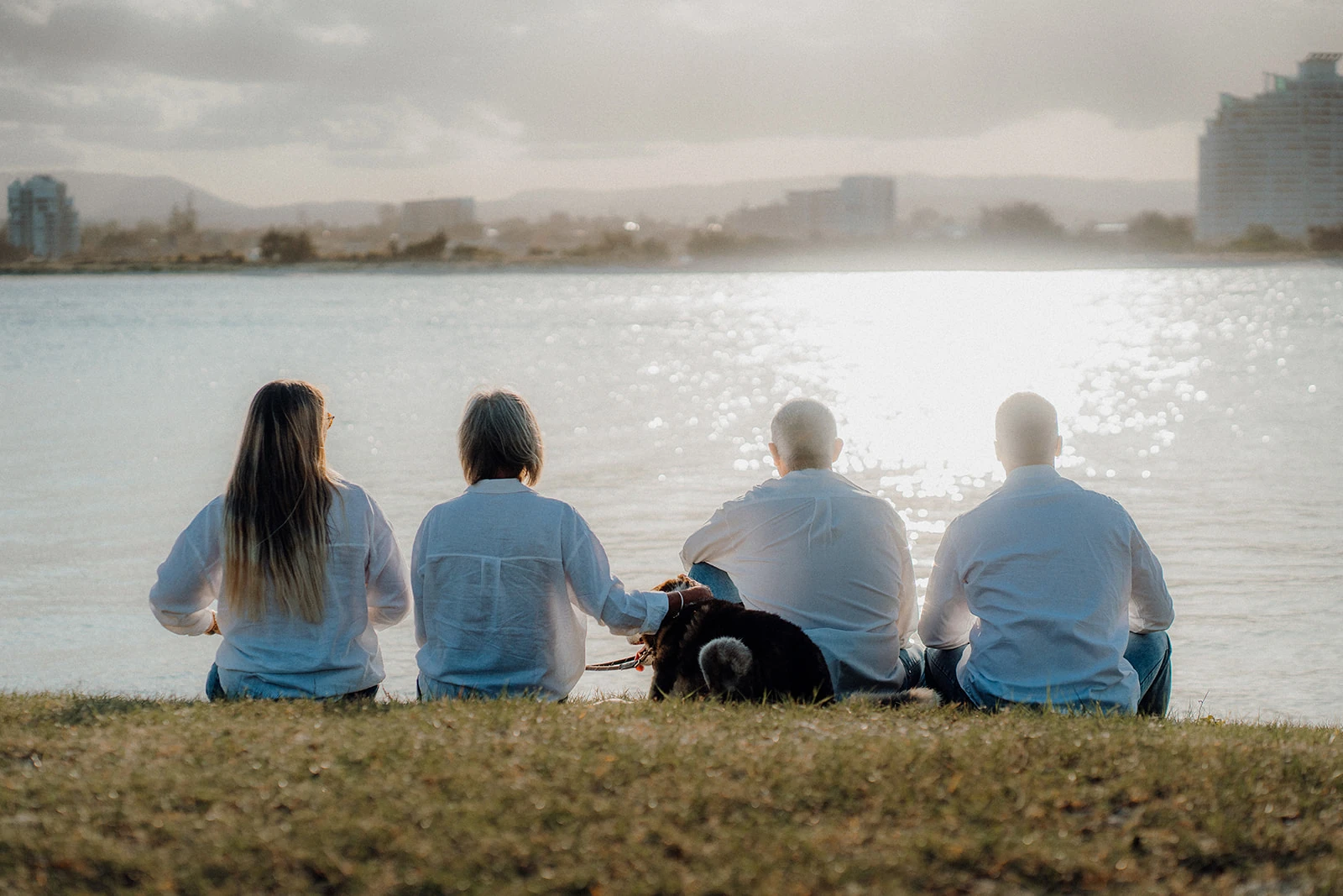 A family and their dog sit facing the sunlit water.