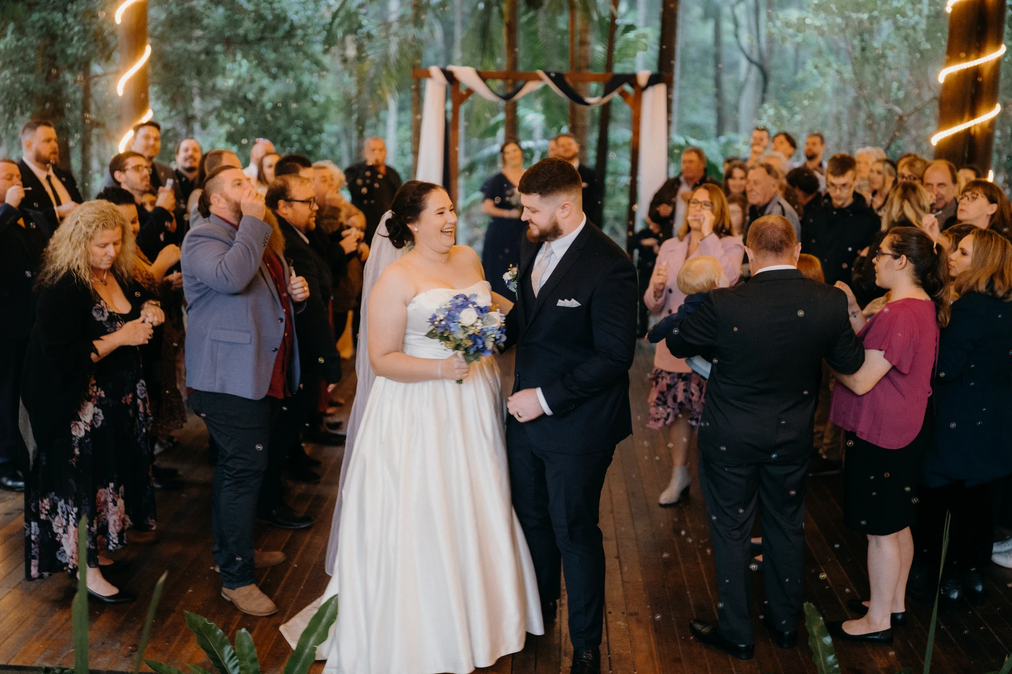 Newlyweds walk between applauding guests in a timber chapel.