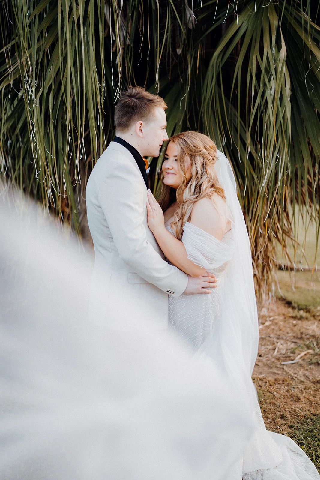 A groom kisses his bride on the forehead behind the sweep of her veil.
