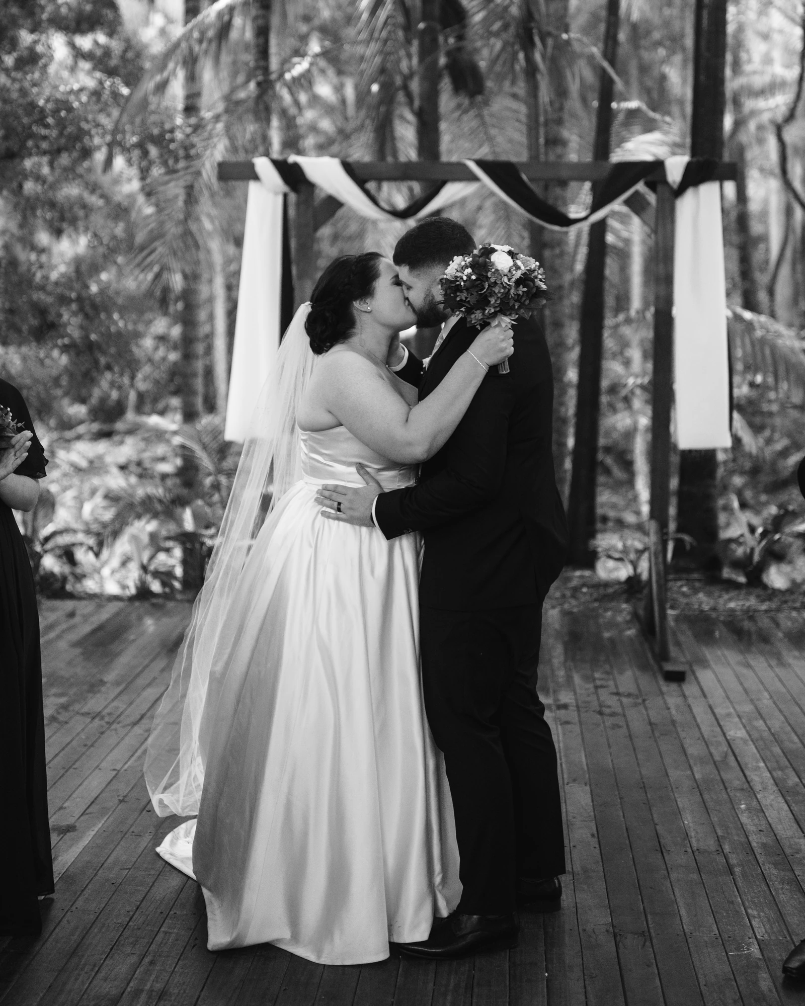 A newly married couple kiss during their ceremony in black and white.