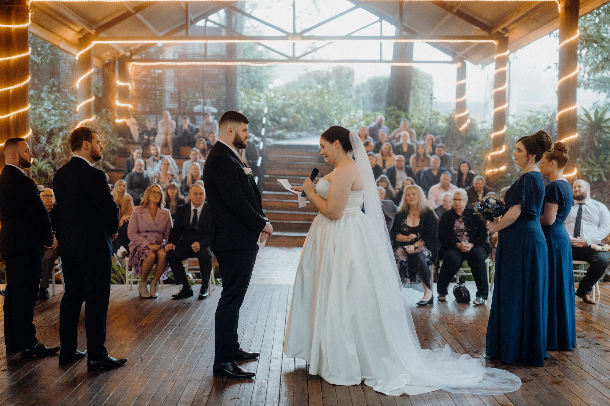A bride reads her vows with guests seated behind the couple.