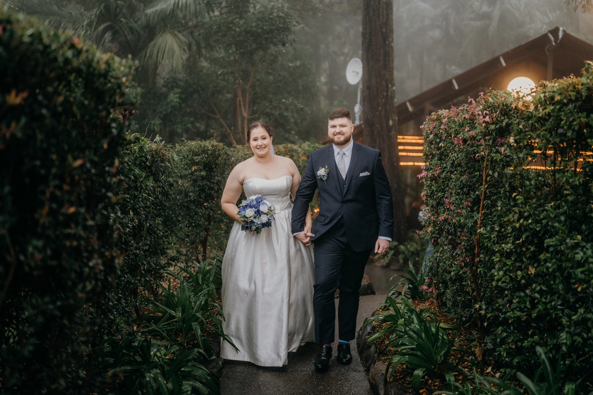 Newlyweds stand together on a garden path beside the chapel.