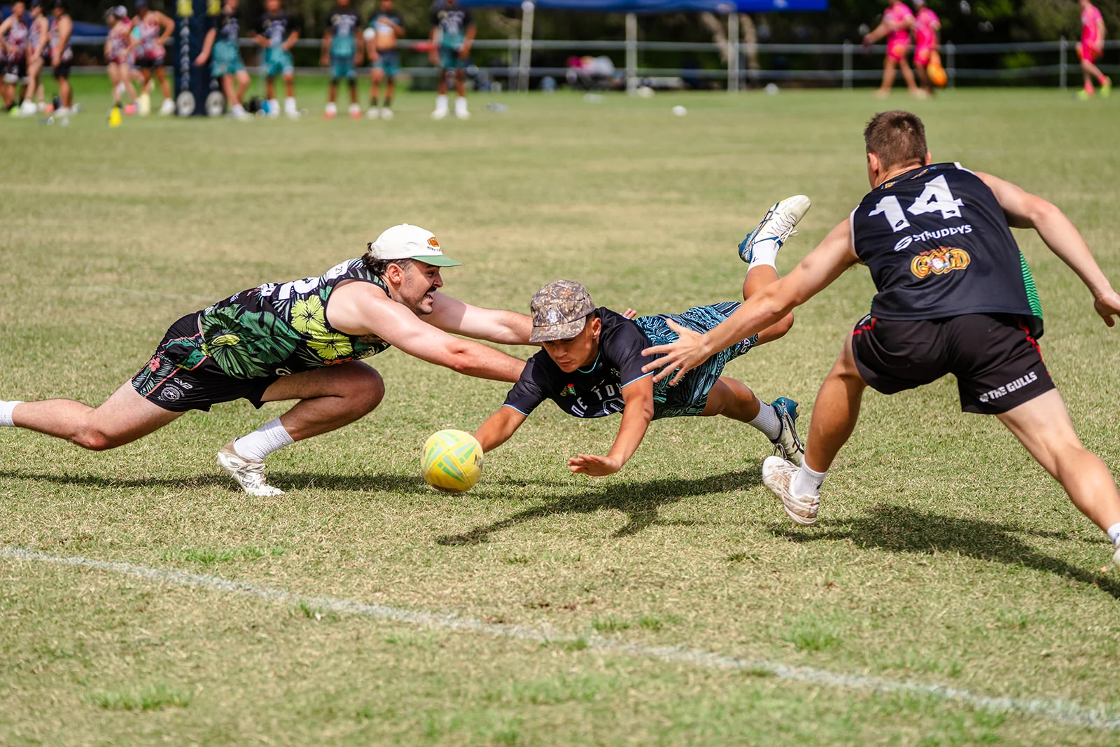 A touch football player dives horizontally between two reaching defenders.