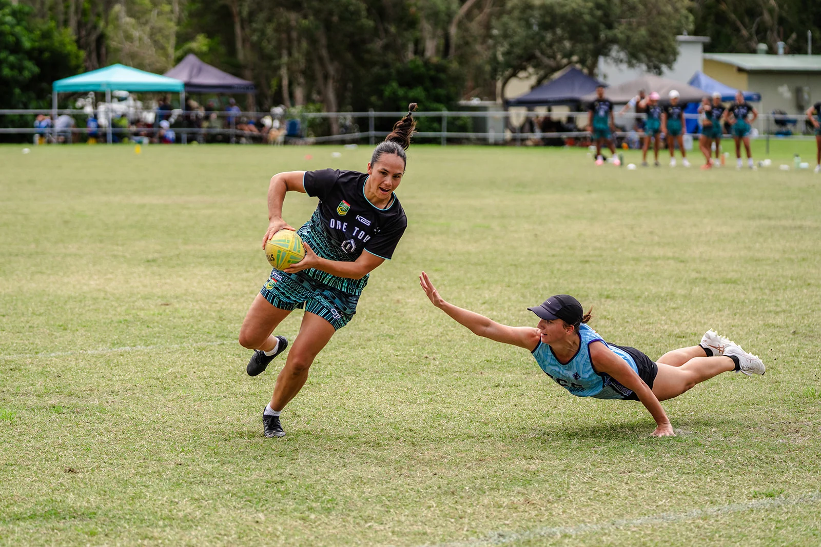 A woman carrying the ball changes direction as a defender dives beside her.