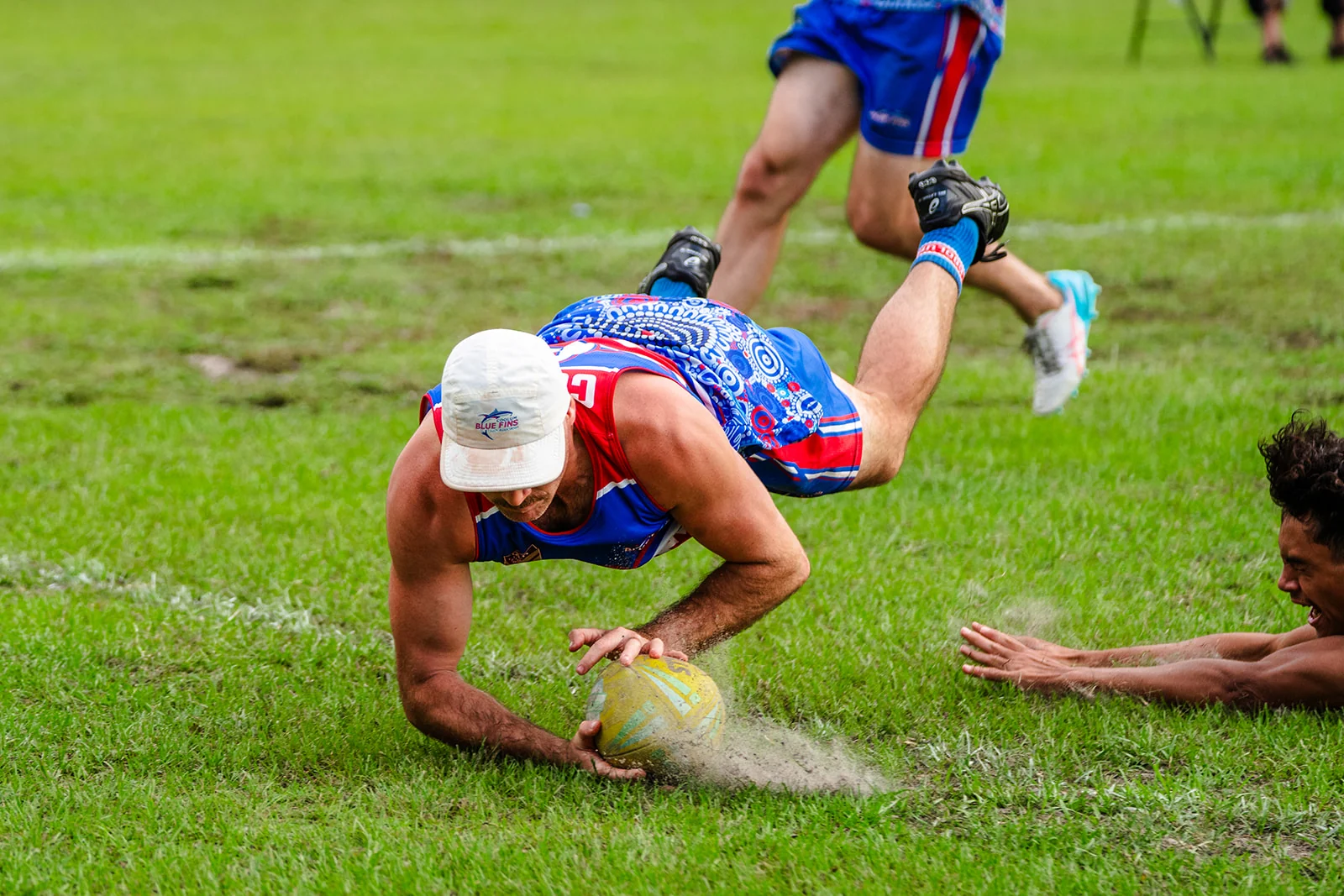 A player in blue dives onto the ball as dust lifts from the turf.