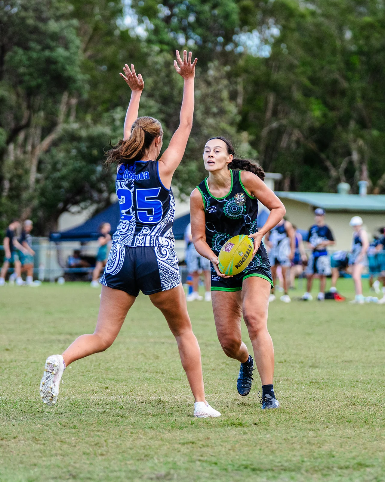 A defender jumps with both arms raised in front of a woman carrying the ball.