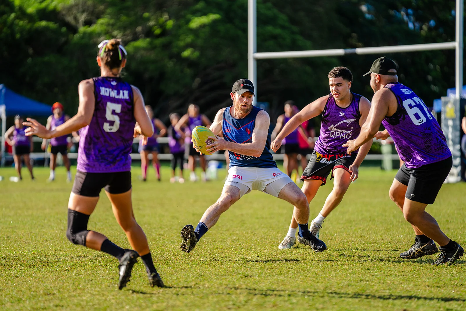 An airborne ball carrier in blue and white steps between purple defenders.