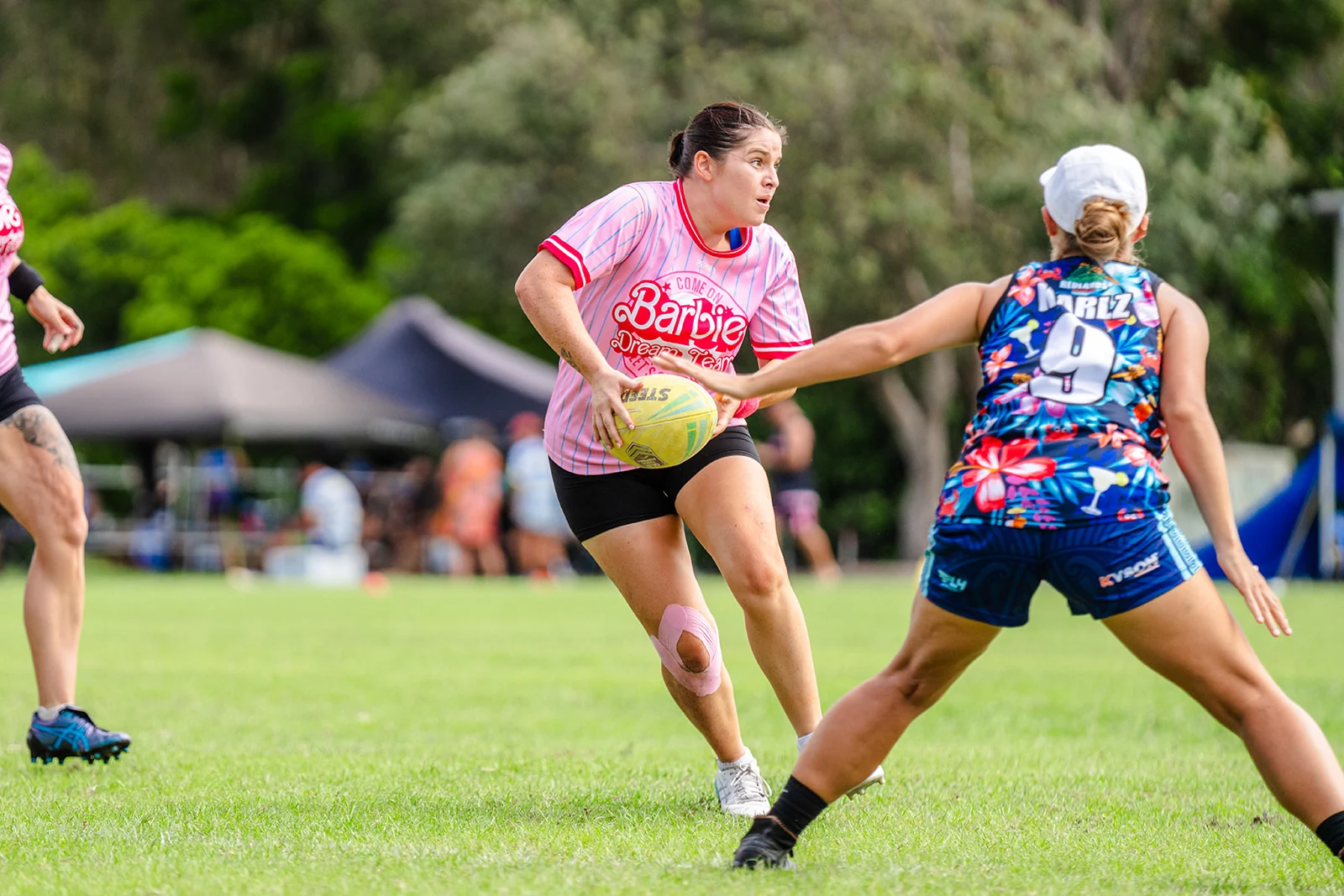 A woman in pink carries the ball past a reaching defender in a floral kit.