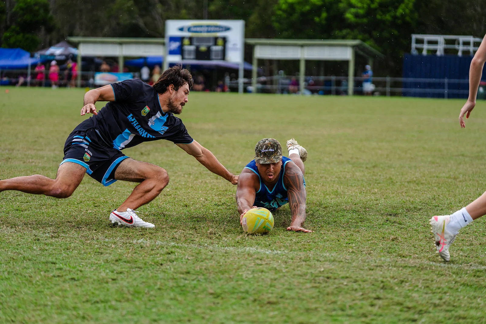 A ball carrier dives forward while a defender reaches across the grass.